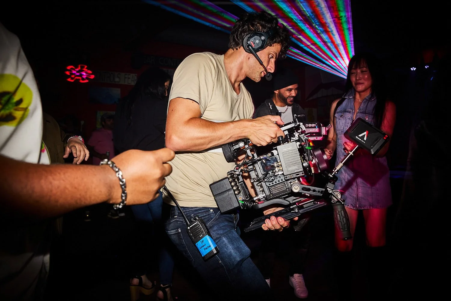 A videographer operating a large professional camera with colorful laser lights in the background.