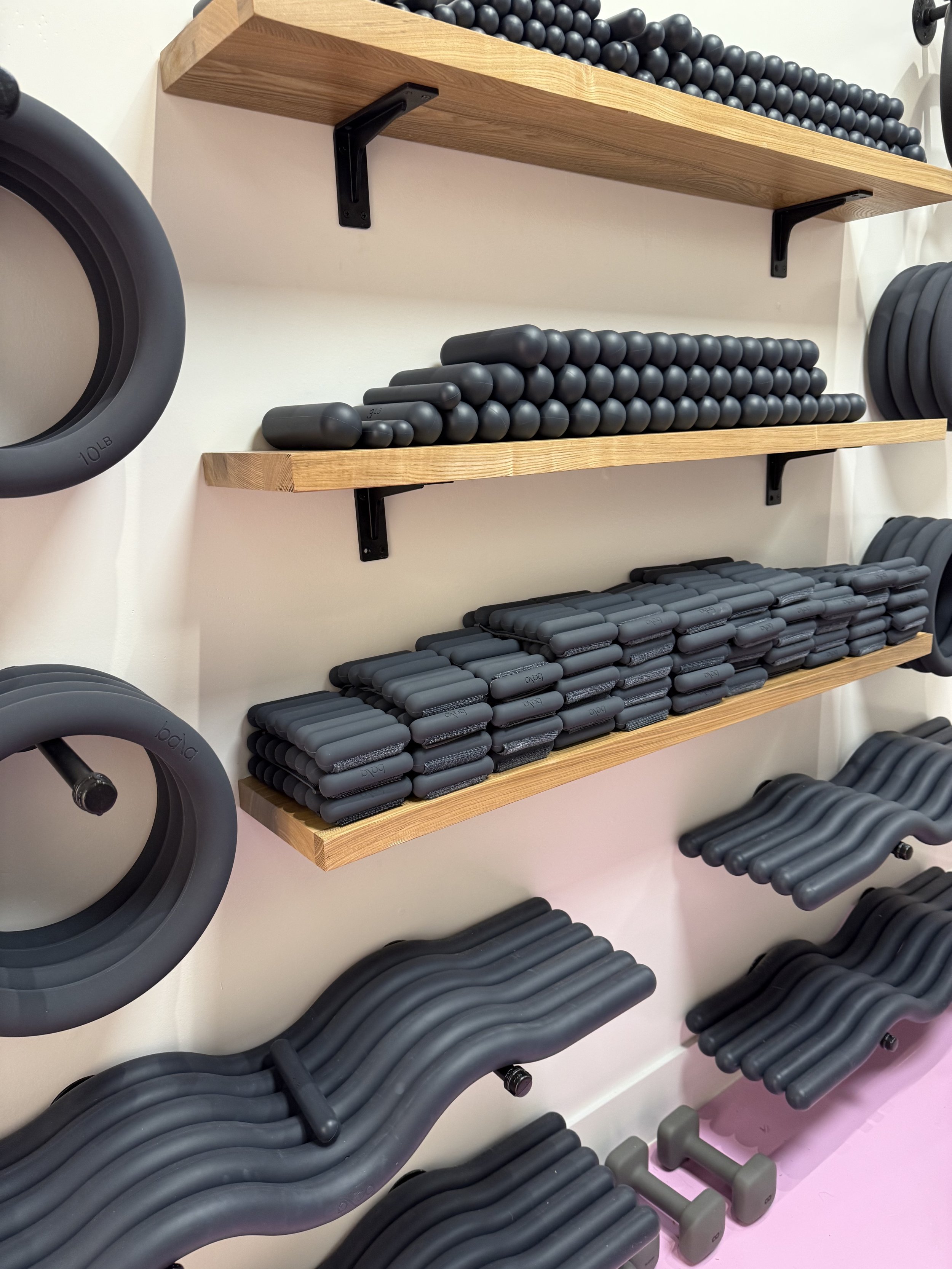 Wooden shelves mounted on a wall holding various black exercise equipment such as kettlebells, dumbbells, and resistance bands in a fitness room.