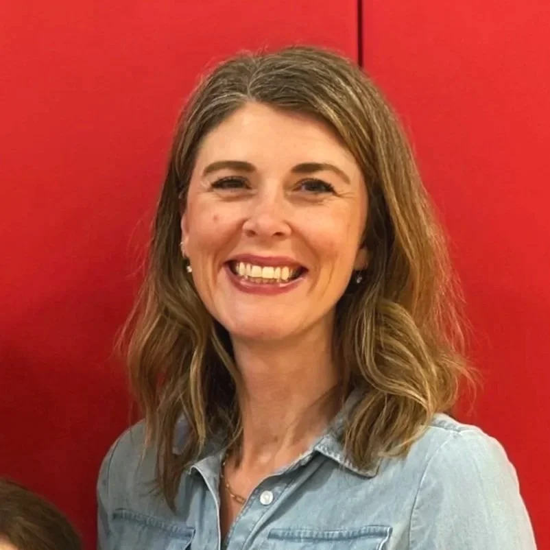 Smiling woman with medium length brunette hair in front of a red wall.