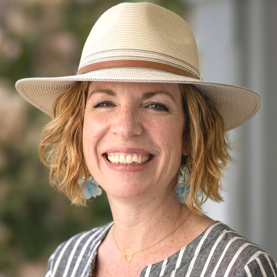 Smiling woman with short, blonde hair and a light tan brimmed hat.