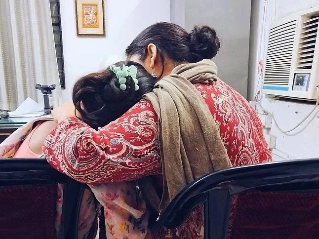 A woman holding another woman in comfort with colorful bold patterned dresses.