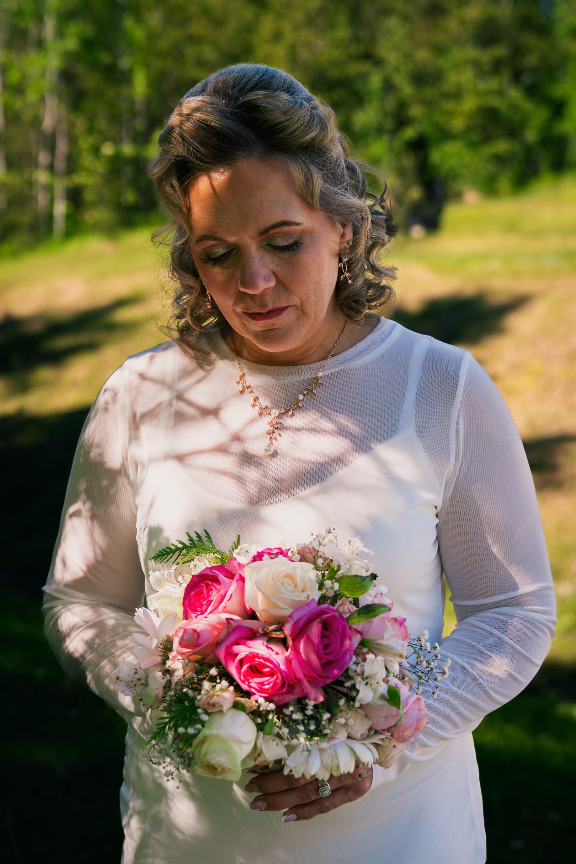 Wedding photo of a bride standing outdoors looking at her bouquet, taken in Prince George, BC