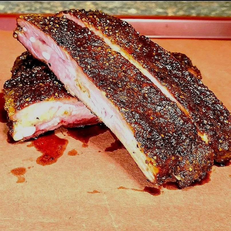 A close-up of a cooked piece of pork rib with a dark, crunchy crust on a cutting board.