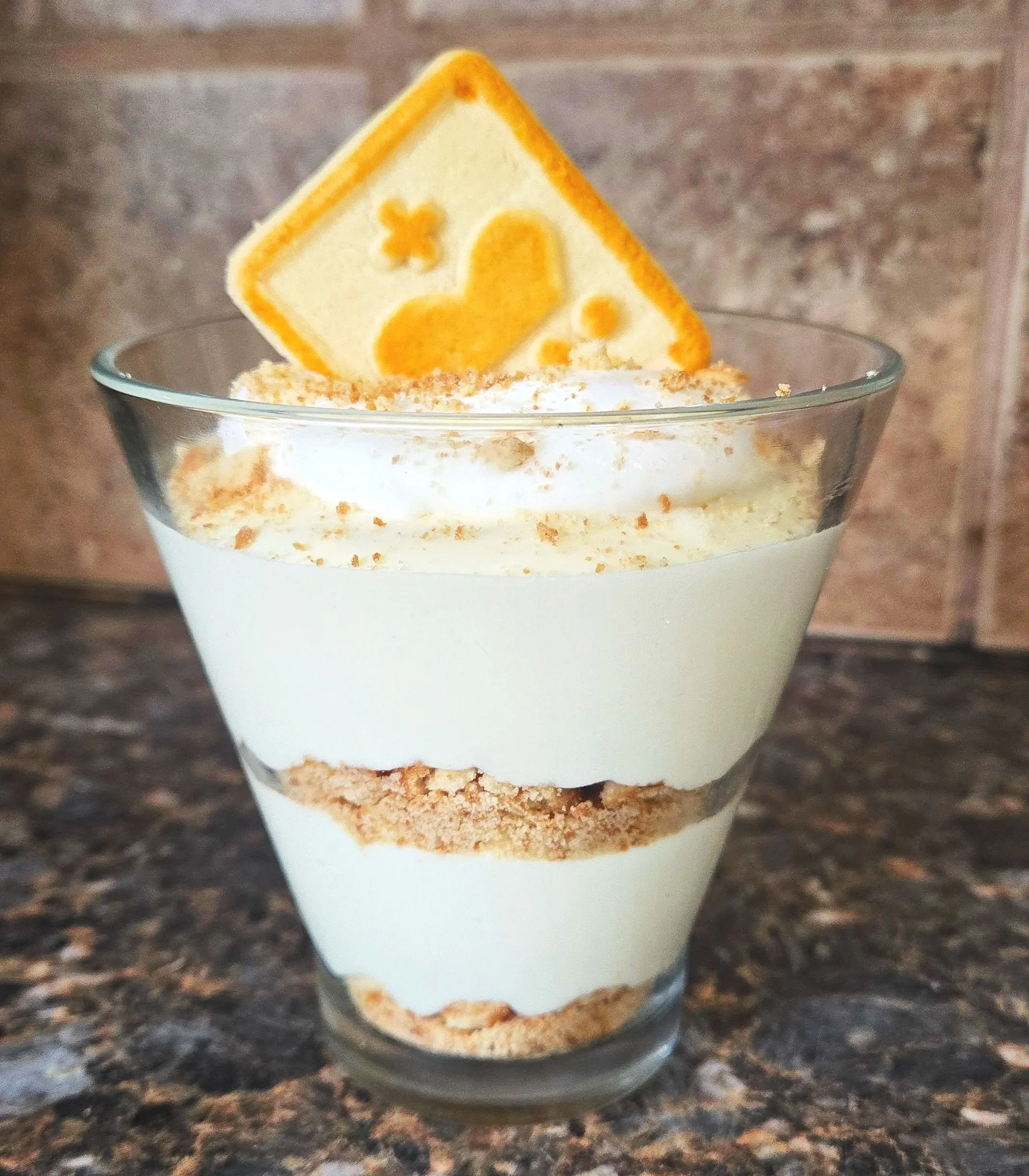 Layered dessert in a glass with cream, cookie layers, and a decorative cracker on top.