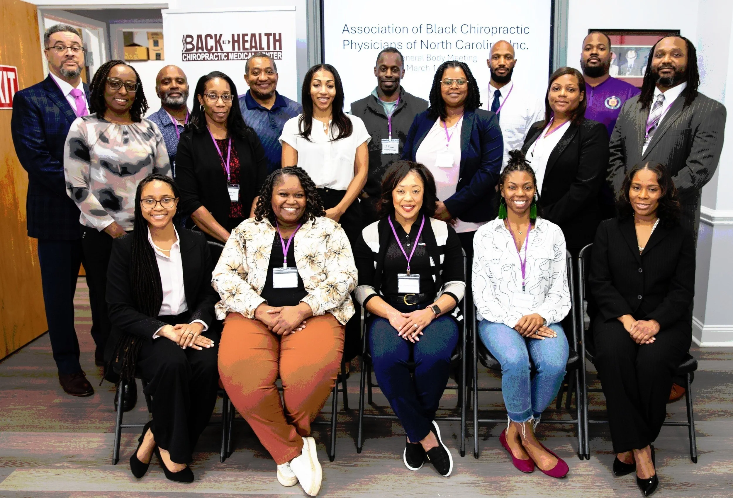 Group of diverse professionals posing for a photo at a chiropractic conference, with a banner in the background displaying the event's name and date.