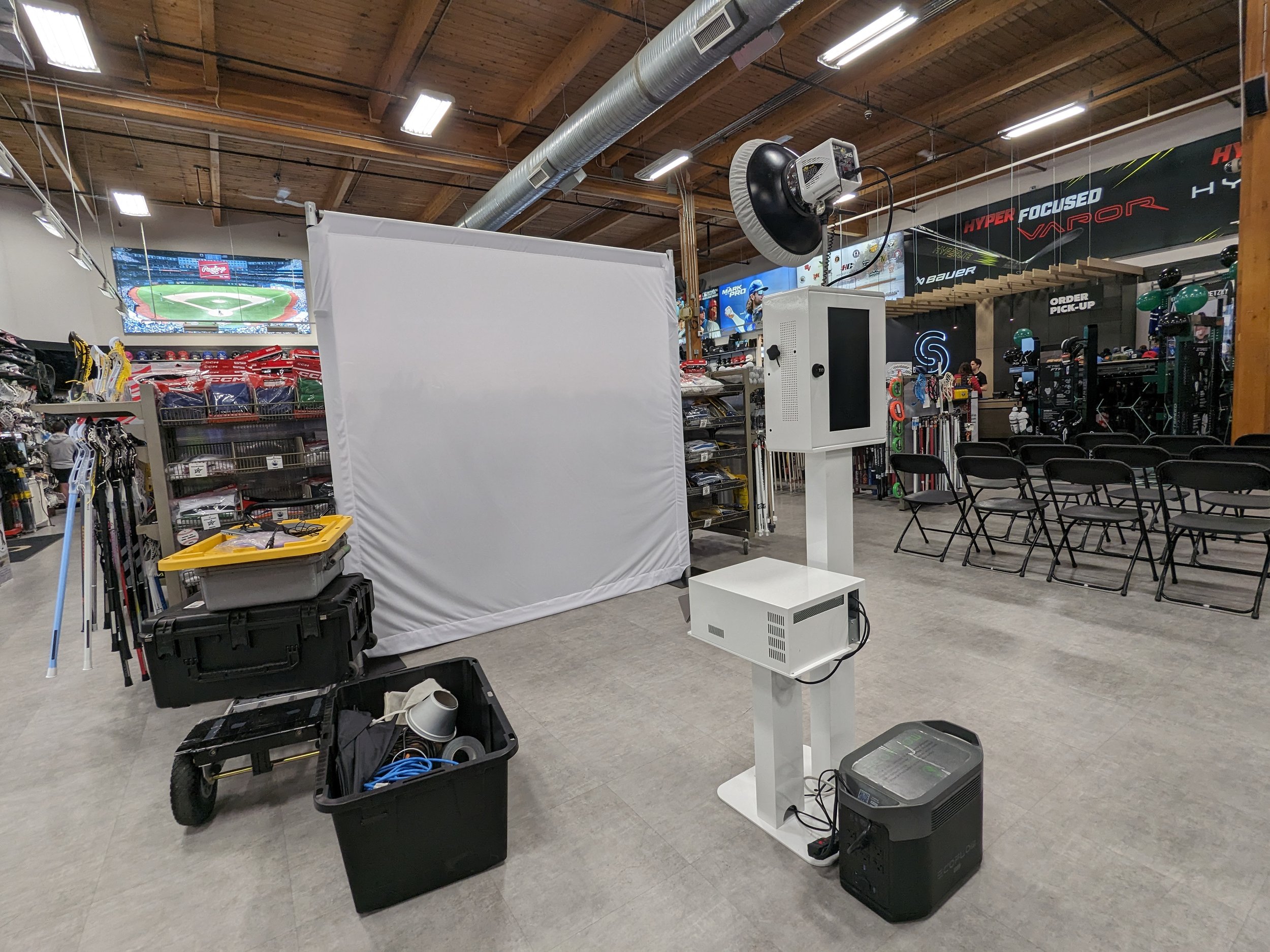 Empty indoor sports equipment store with white screen, chairs, and storage boxes, possibly set up for an event or presentation.