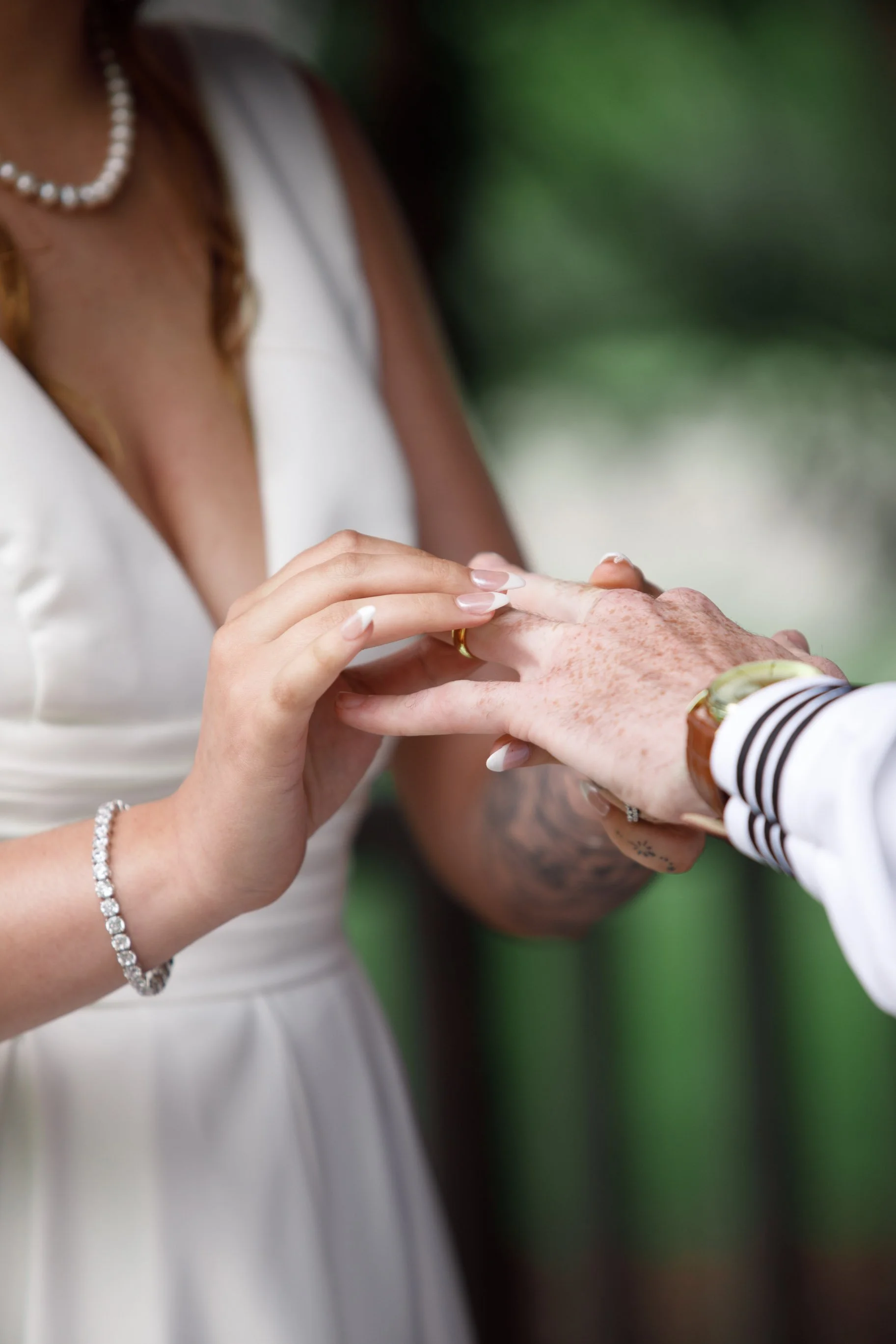 A woman placing a ring on a man's finger during a wedding ceremony, with a blurred background.