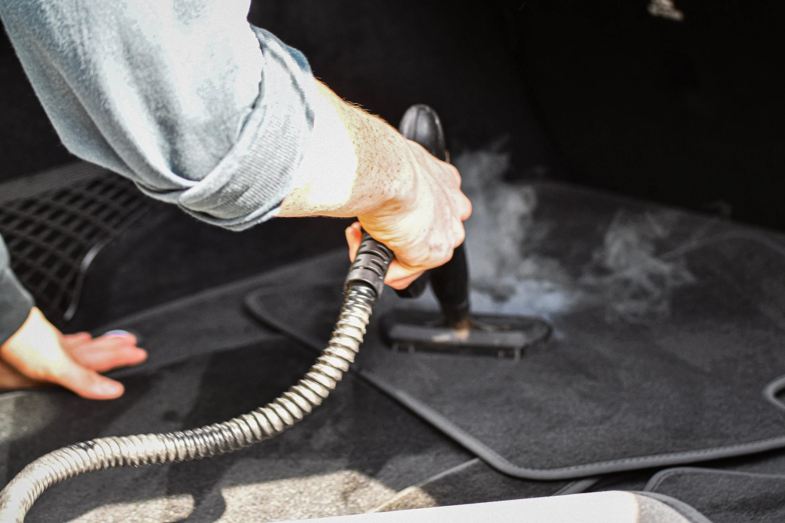 Person vacuuming car floor mats with a handheld vacuum cleaner.