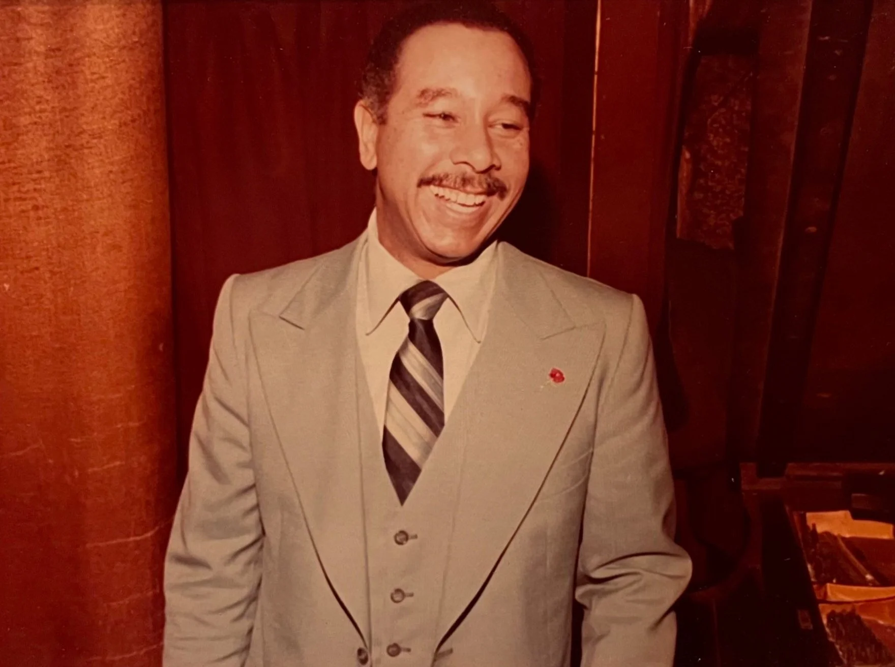Vintage portrait of a smiling man with a mustache wearing a light-colored suit and striped tie.