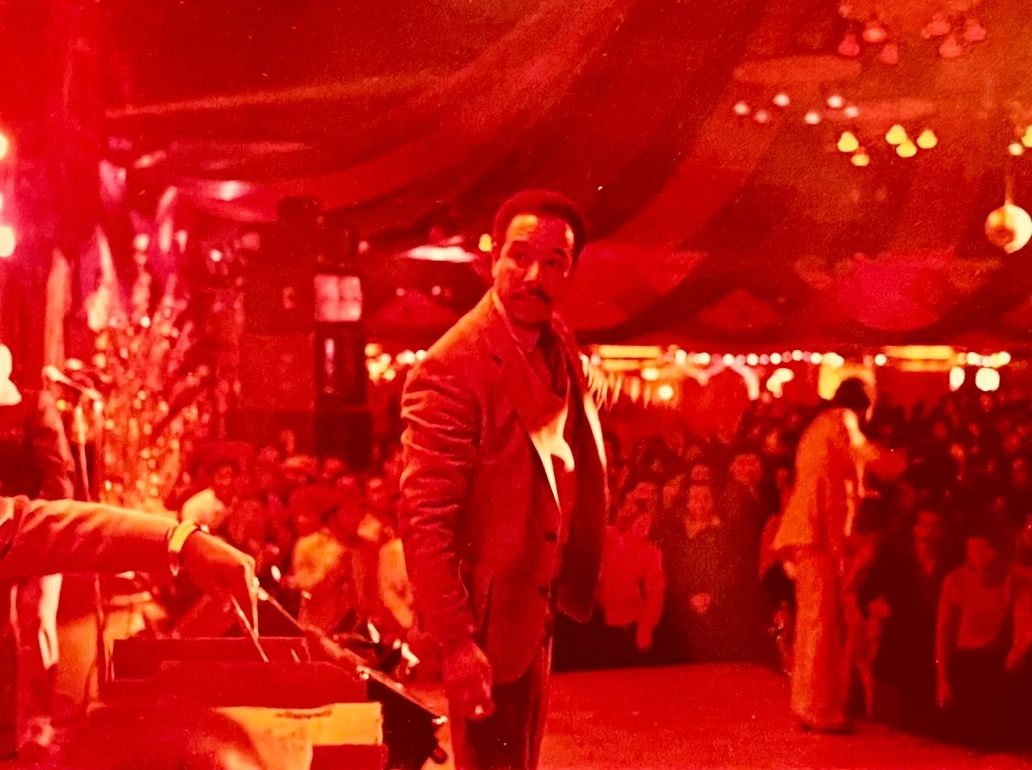 Man in a suit standing amid a crowded, warmly lit indoor venue