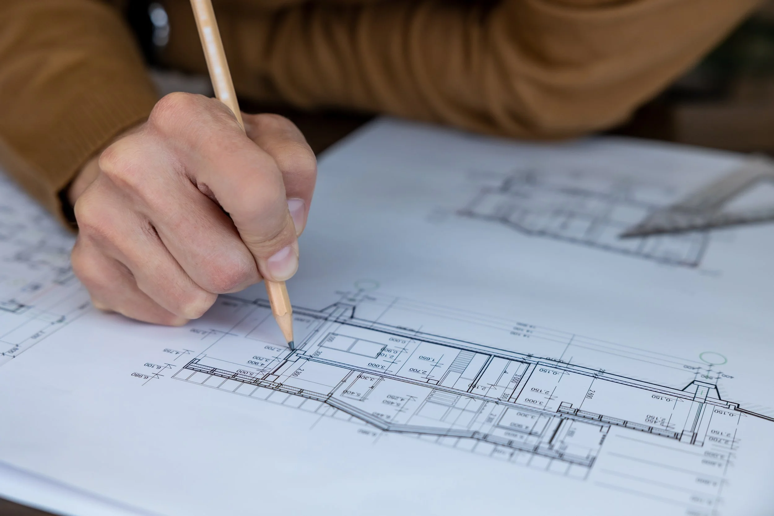 A person using a pencil to mark or draw on a detailed architectural blueprint or floor plan.