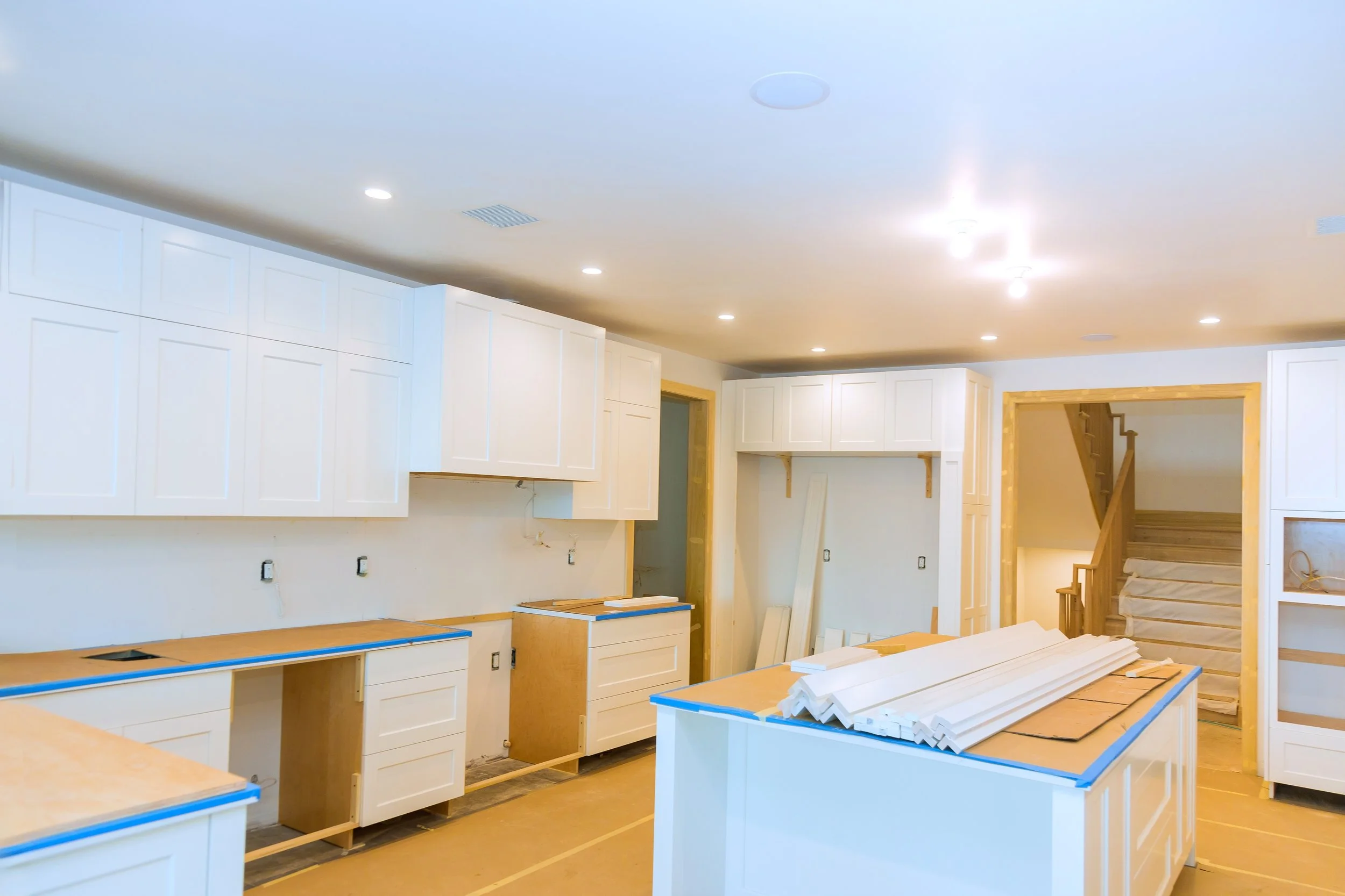 Kitchen under construction with white cabinets, wooden countertops, and a staircase in the background.