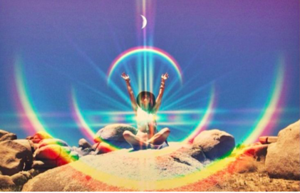 Person sitting cross-legged on rocks at sunset, with hands raised, surrounded by colorful rainbow-like light patterns and a crescent moon in the sky.