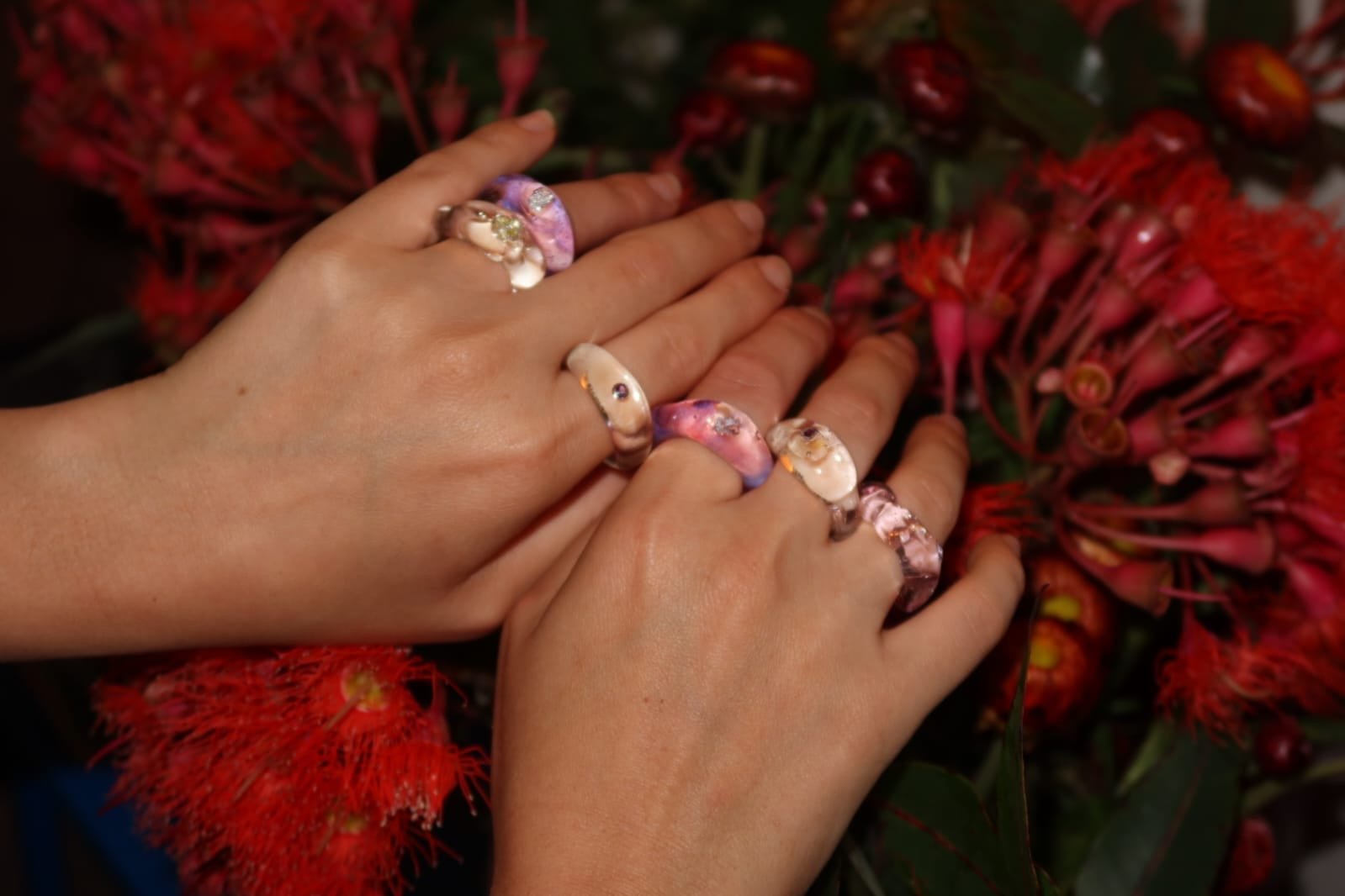 Two hands with glass rings resting on red flowers with long stamens.
