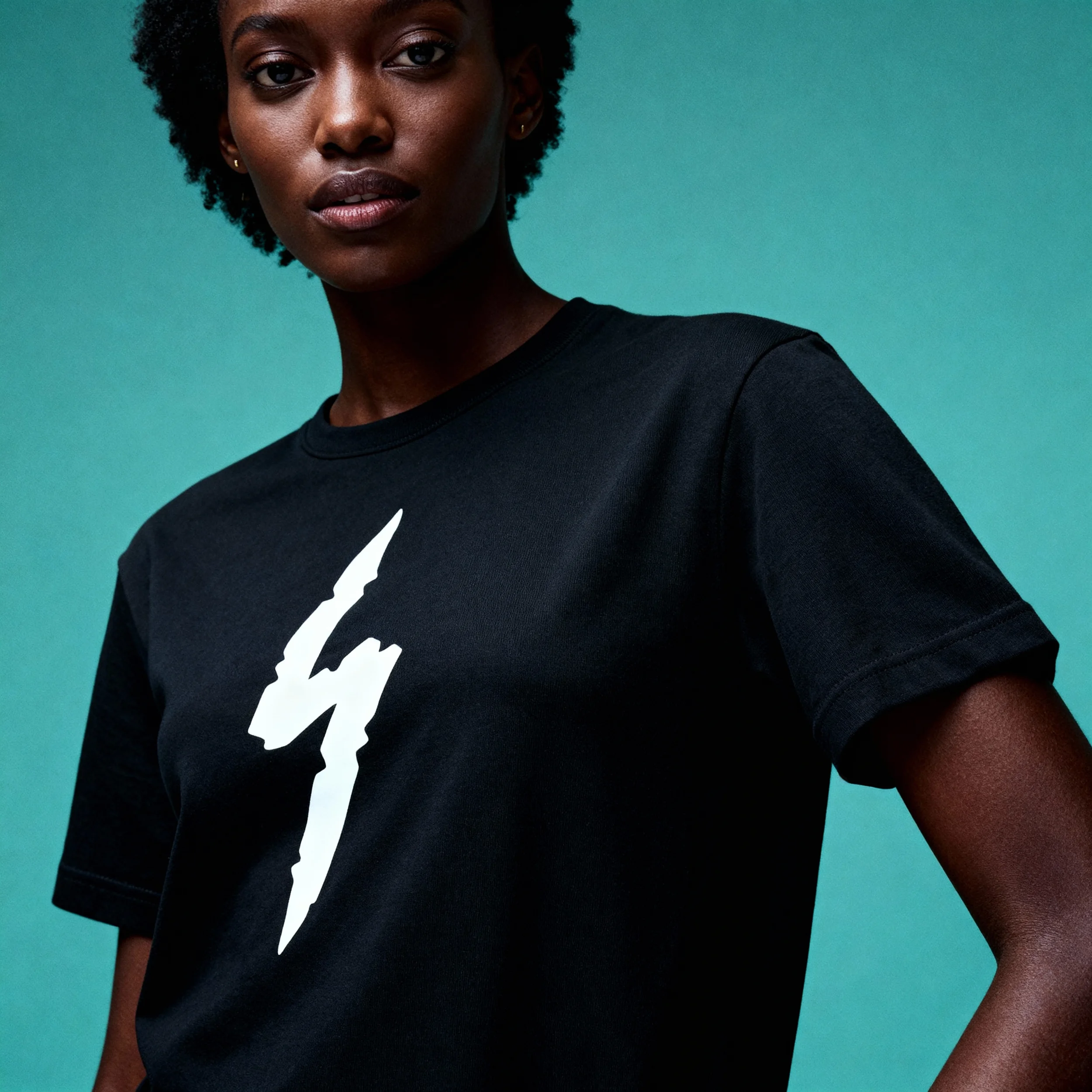 Close-up of a woman wearing a black T-shirt with a white lightning bolt graphic, against a teal background.