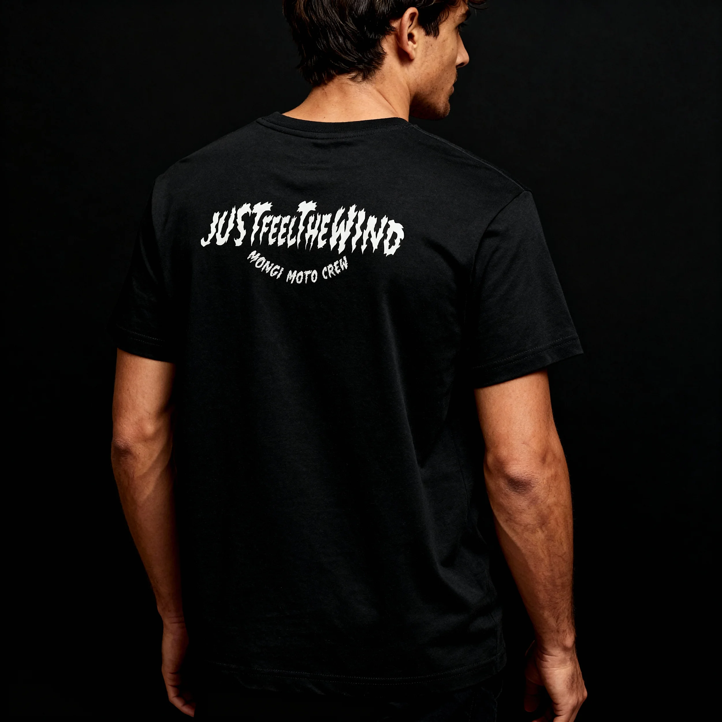 Back view of a man wearing a black T-shirt with white text that says 'JUST FEEL CHEING' and 'WONGLI MOTO CREW' on the back, against a black background.