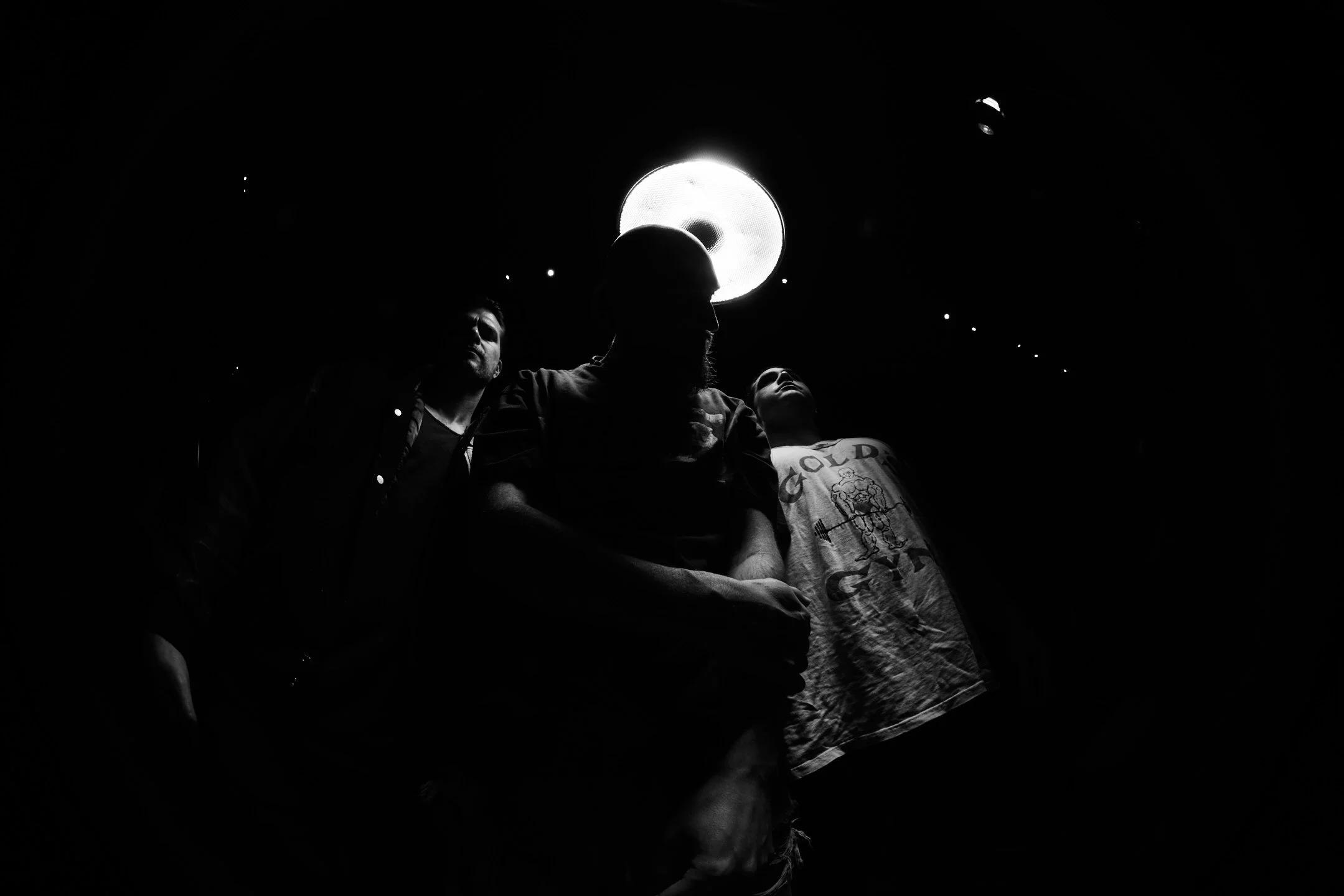 Three men standing together in front of a bright circular light source, with the photo taken from below, creating a silhouette effect.