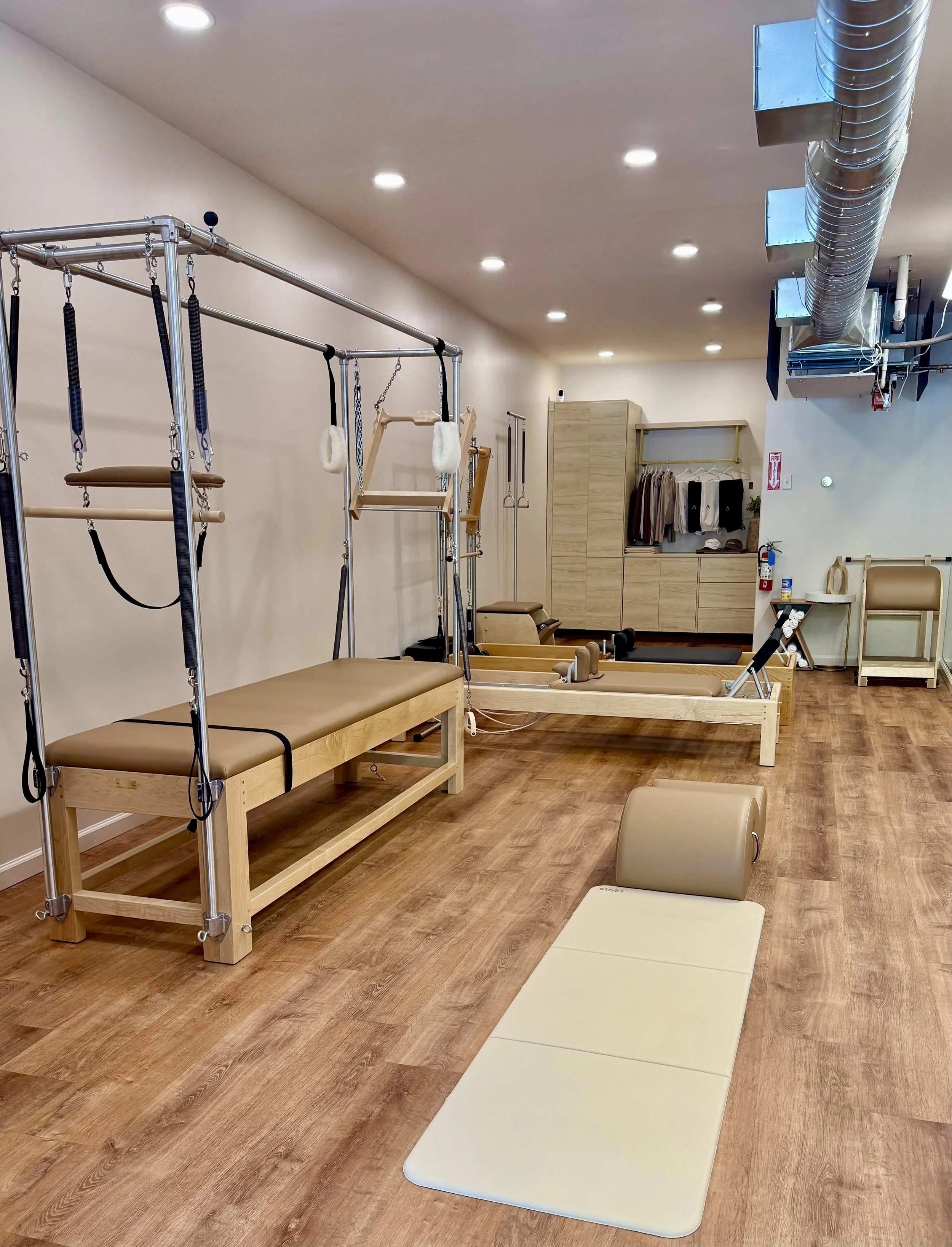 A pilates studio including a Cadillac, mat, two reformers, spine corrector, and ladder barrel with mirror on wall and wooden floors