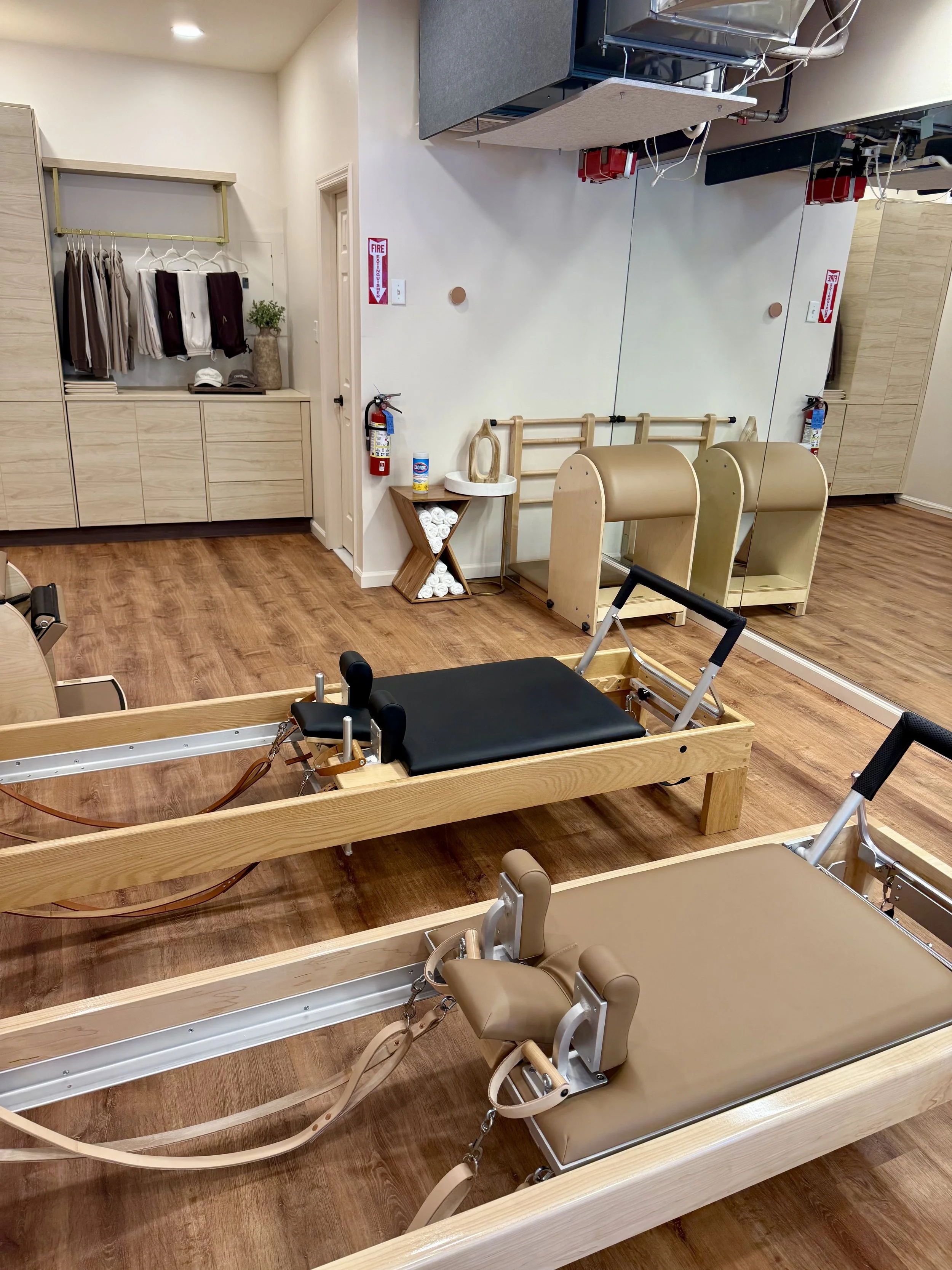 Pilates studio with two reformers, wunda chair, and ladder barrel, mirror on wall, and wooden floors.
