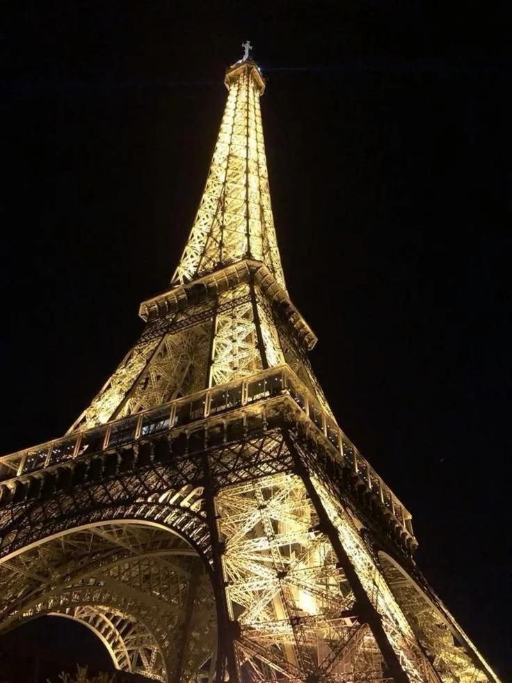 The Eiffel Tower illuminated at night, glowing with golden lights against a dark sky.