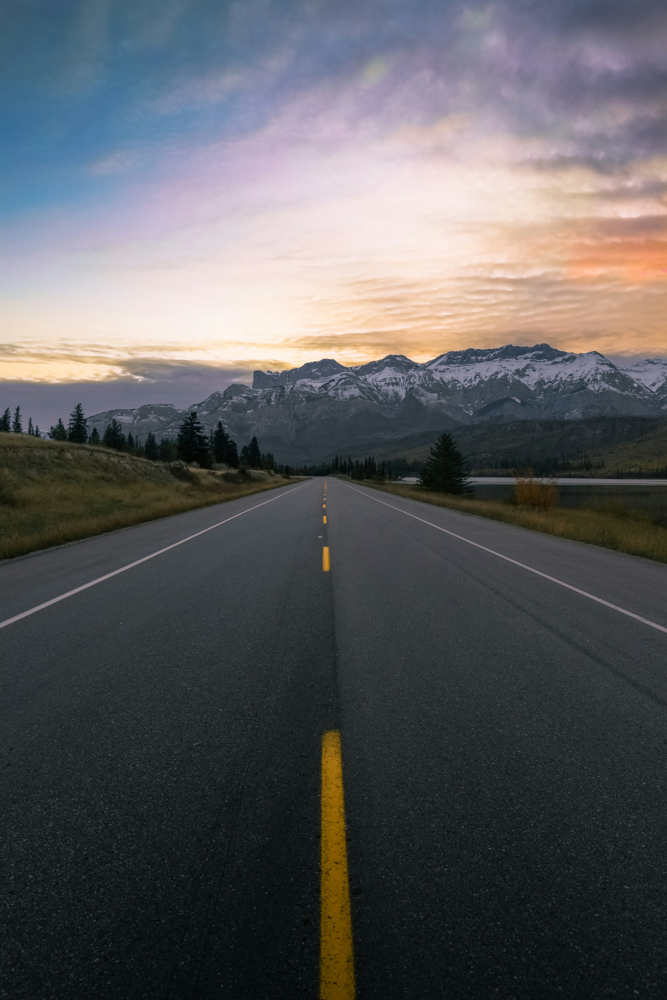 Open road leading toward snow-covered mountains at sunrise.