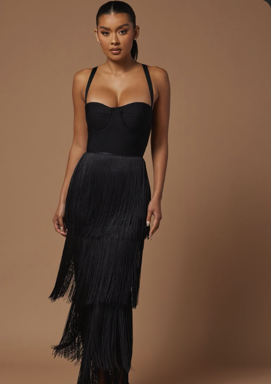 A woman wearing a black strapless corset top and a high-waisted, layered fringe black skirt posing against a neutral background.