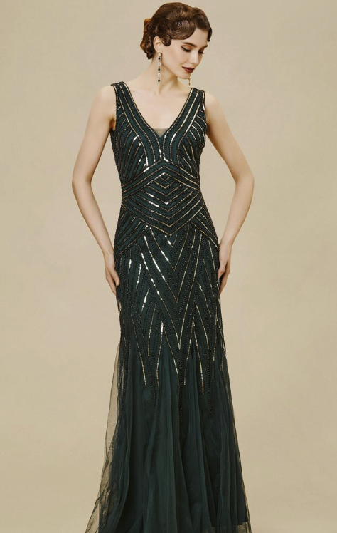 A woman in a dark green, sequined evening gown with geometric patterns, standing against a beige background.