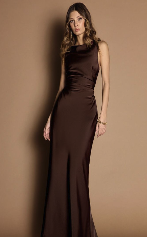 Woman wearing a long, brown satin evening gown with sleeveless design and a high neckline, standing against a beige background.