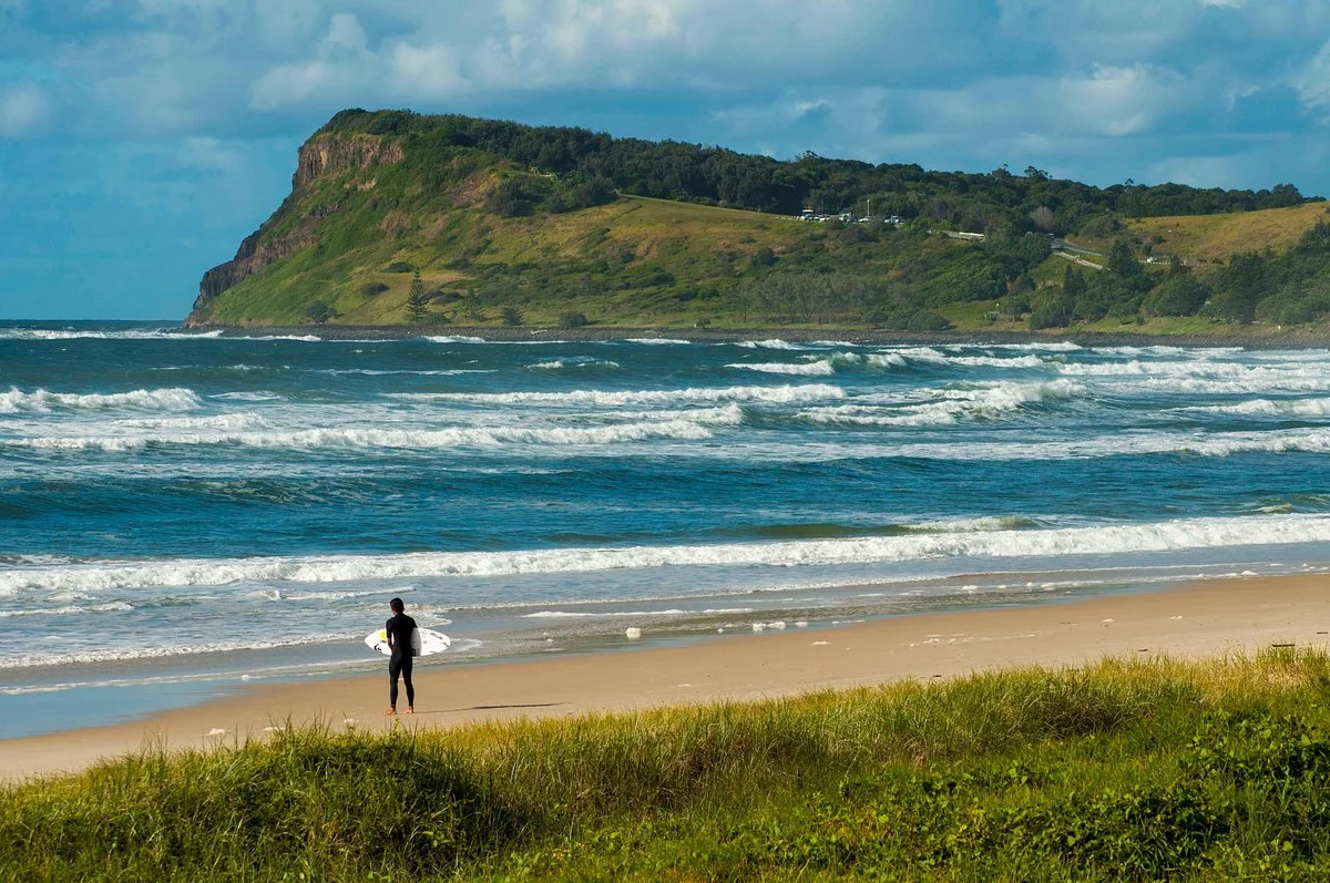 Surfer on Lennox Head NSW beach with hills in the background, an Oke Building service area