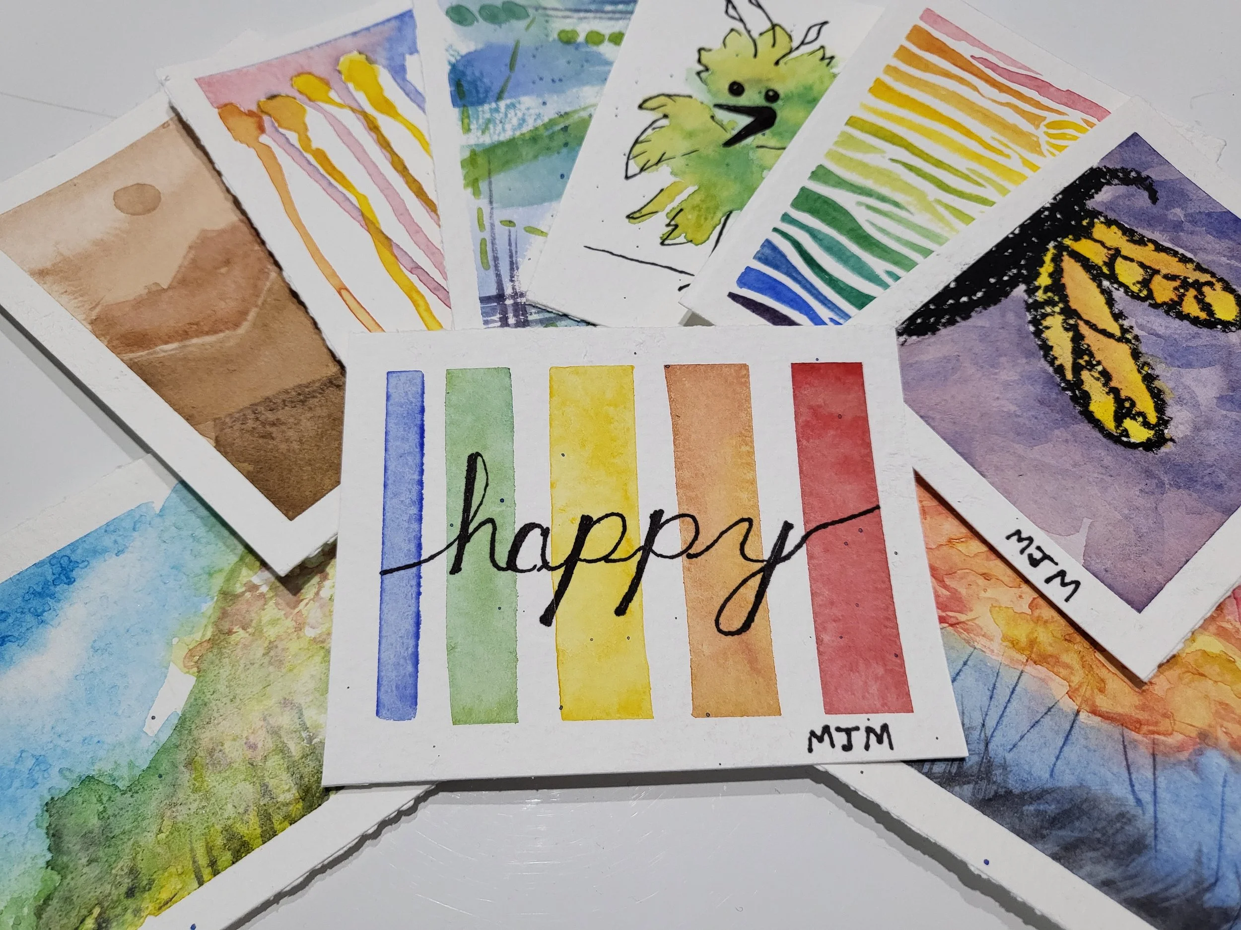 Collection of colorful watercolor art cards, including a rainbow with the word 'happy' written across, a bee, a chick, and abstract patterns.