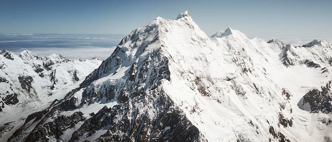 Snow-covered mountain range with a prominent peak under a clear sky.