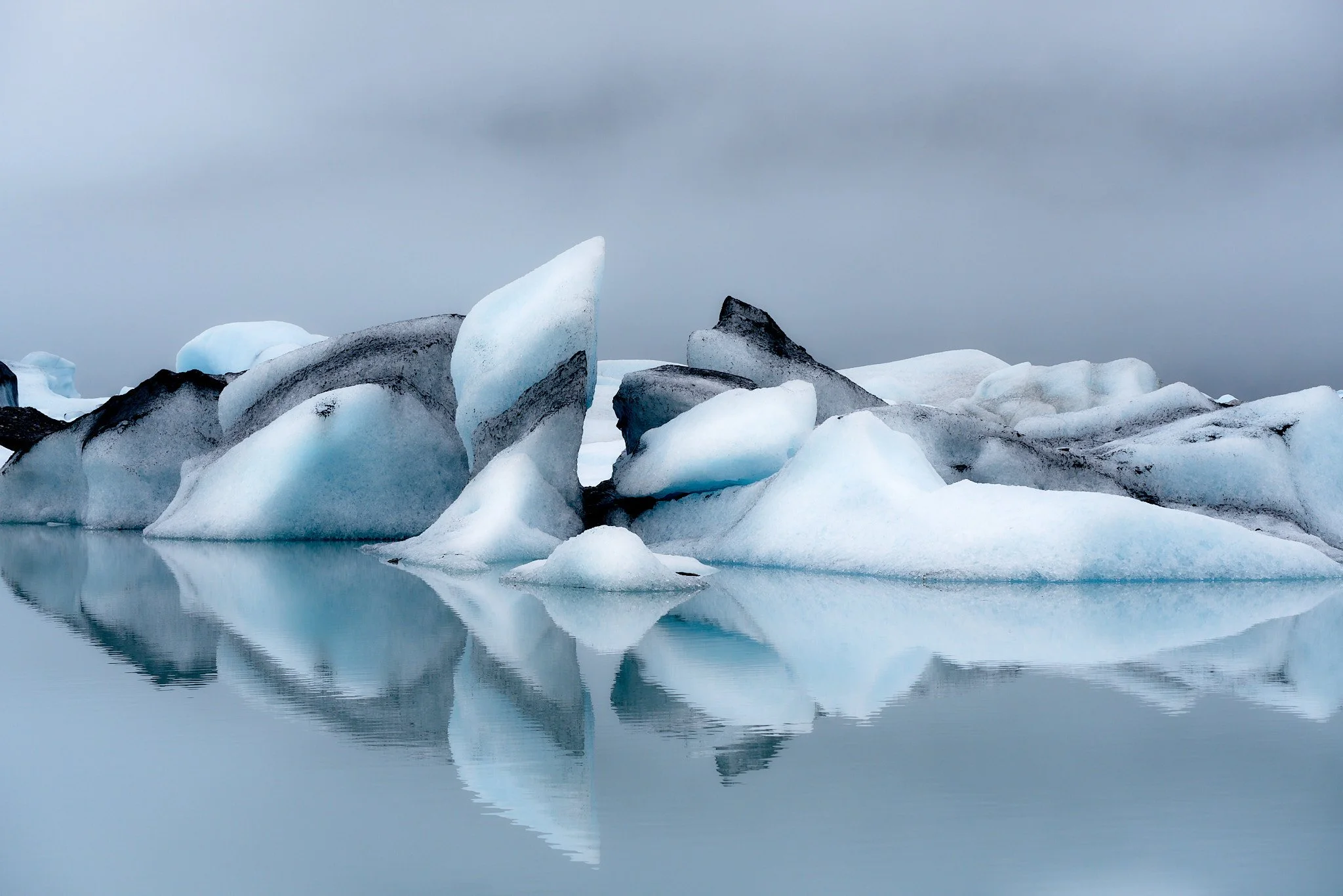 Icebergs floating on calm water with a cloudy sky in the background.