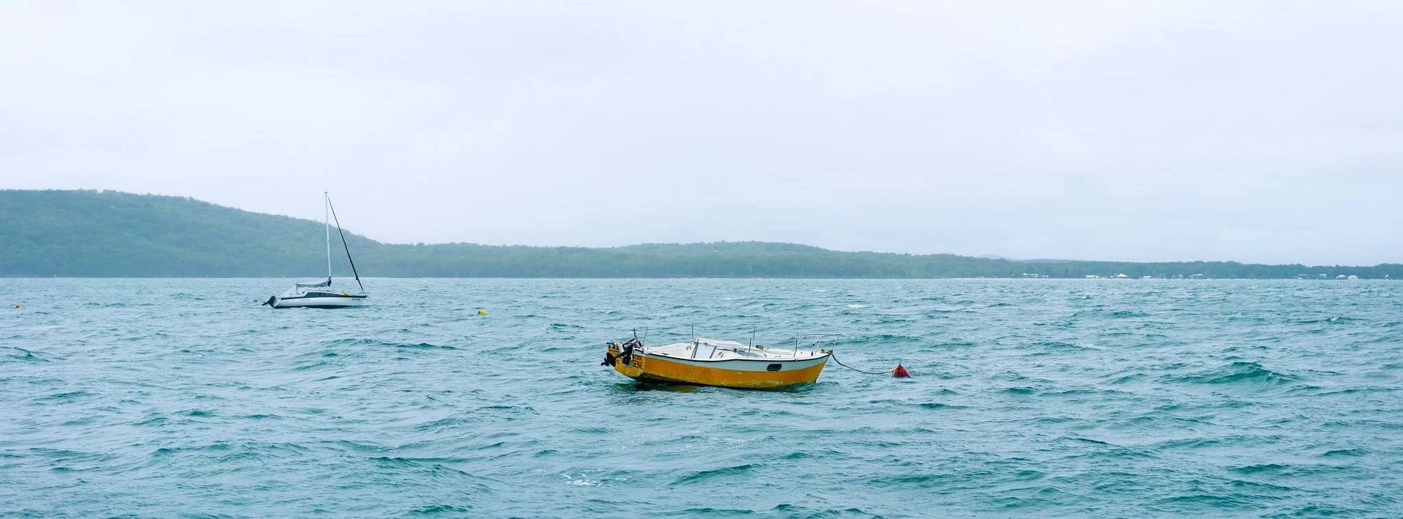 Two boats floating on a body of water with hills in the background on a cloudy day.