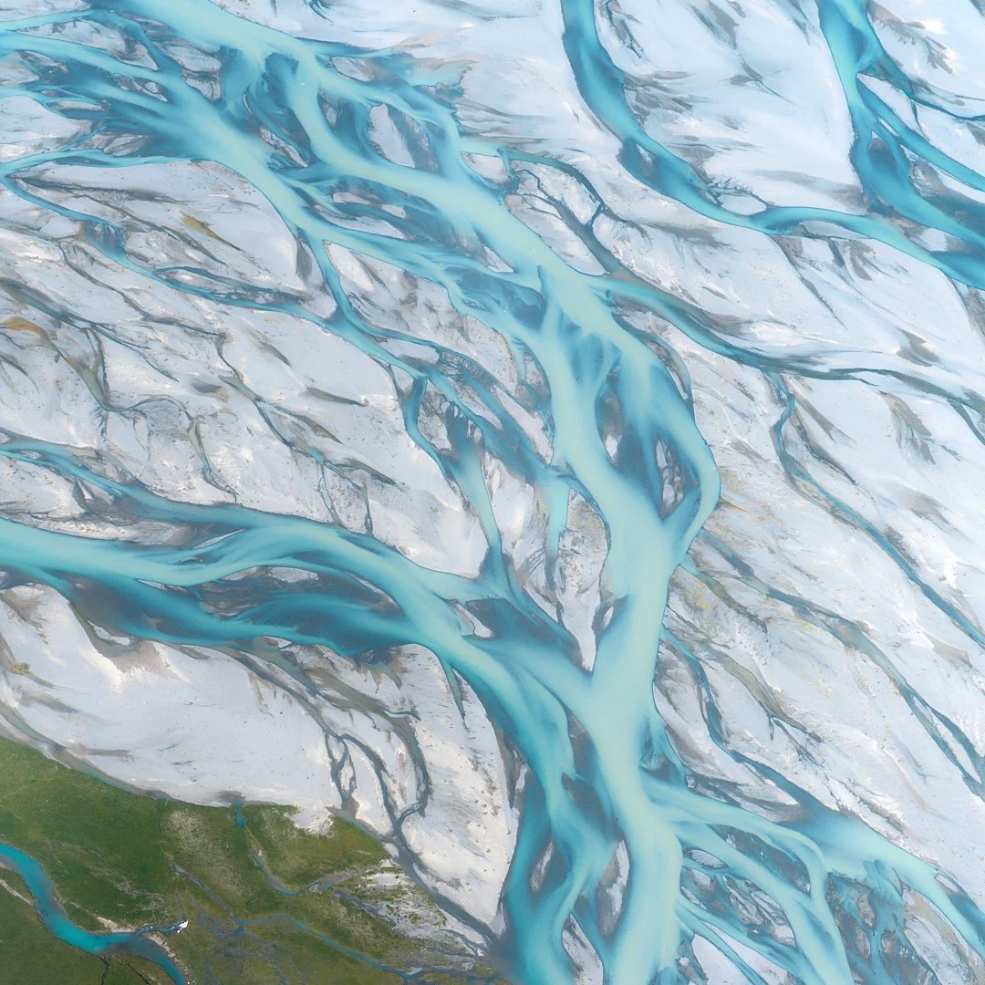 Aerial view of a glacier with bright blue meltwater streams flowing through the ice and some green land at the bottom.