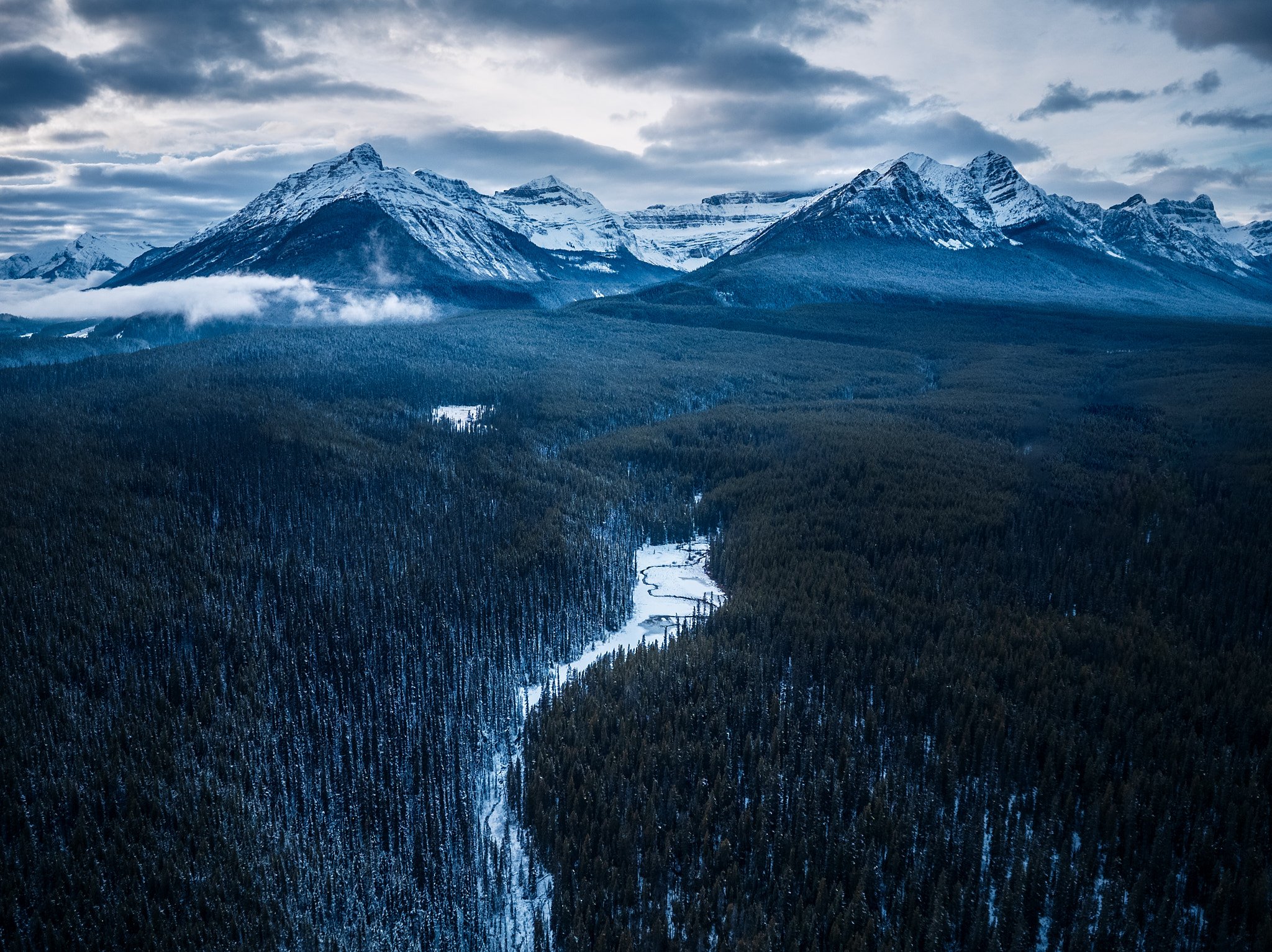 Snow-capped mountains over a dense forest with a winding river in the valley
