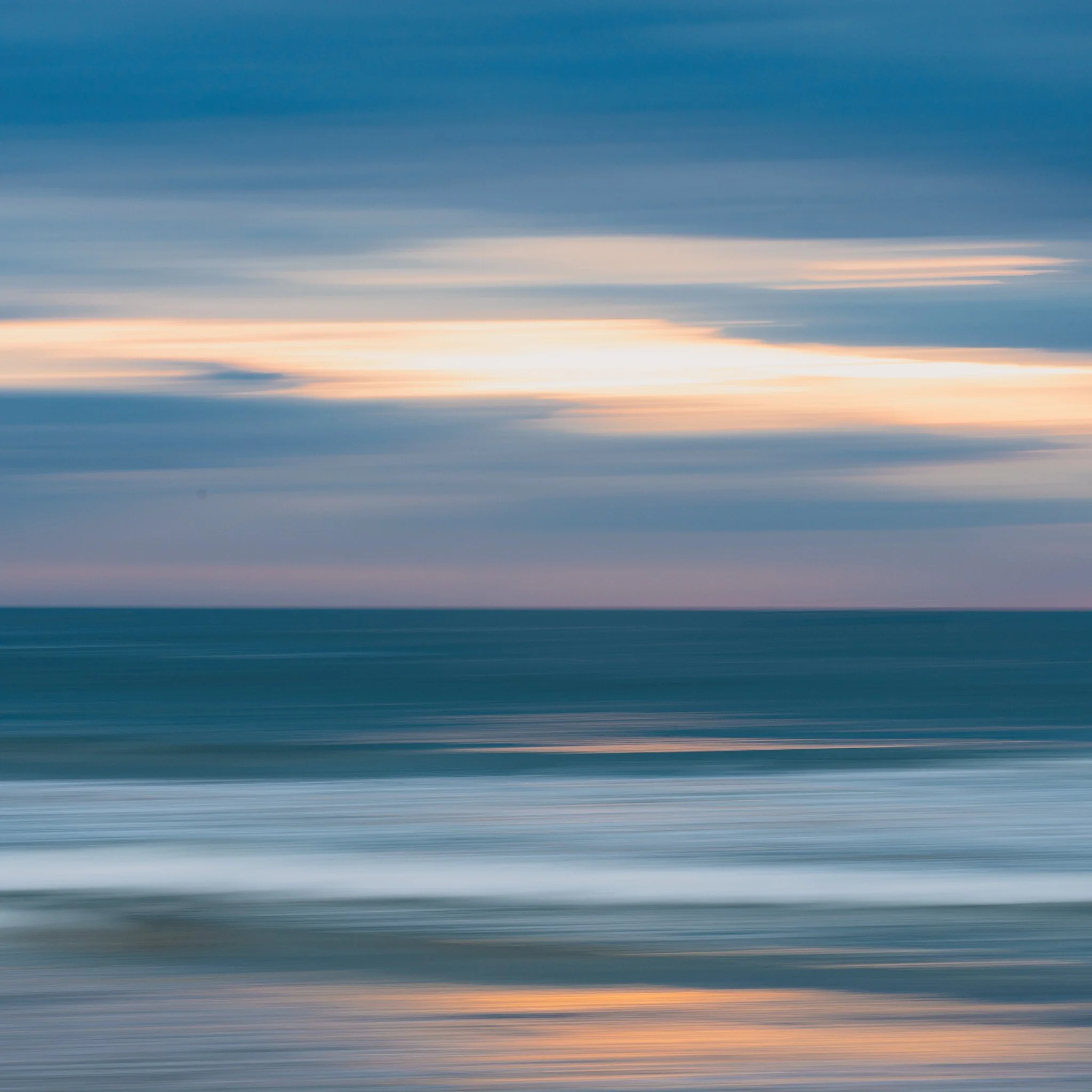 Abstract photo of the ocean with motion blur, showing waves and a cloudy sky at dusk or dawn.