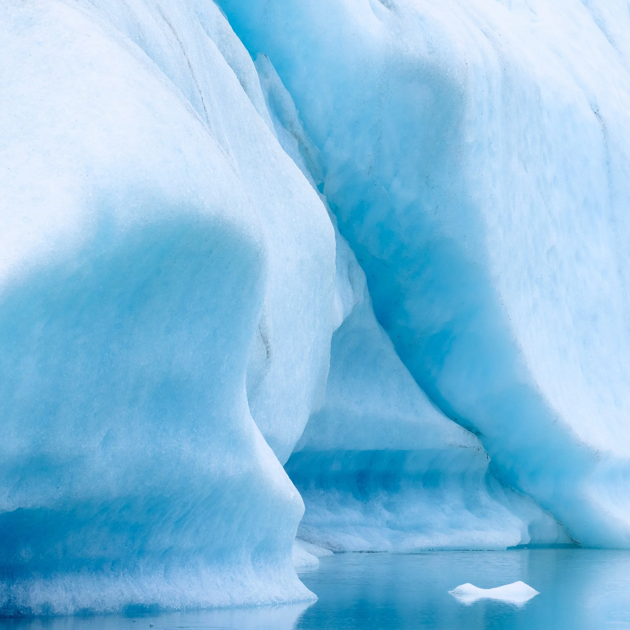 Close-up of a blue ice glacier with a small chunk of ice floating in the water.
