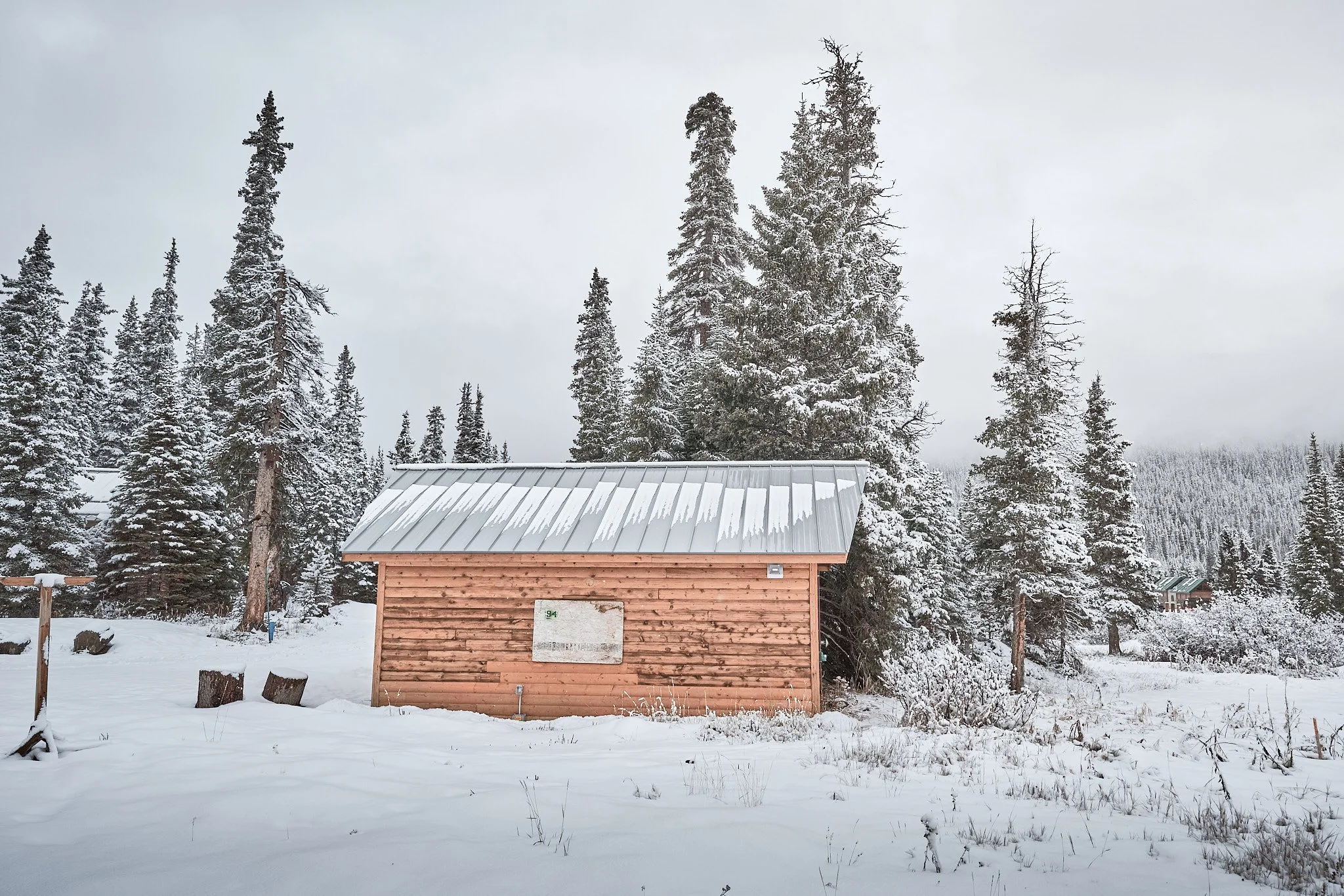 A small wooden cabin with a metal roof surrounded by snow-covered trees in a winter landscape.