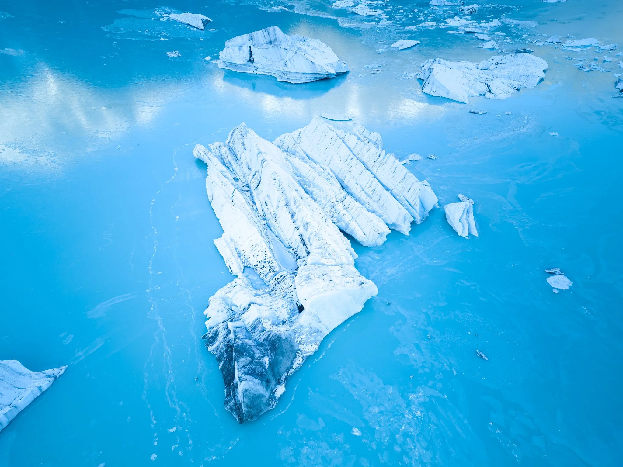 A landscape of icy glaciers and frozen water with large ice chunks floating in a cold blue environment.