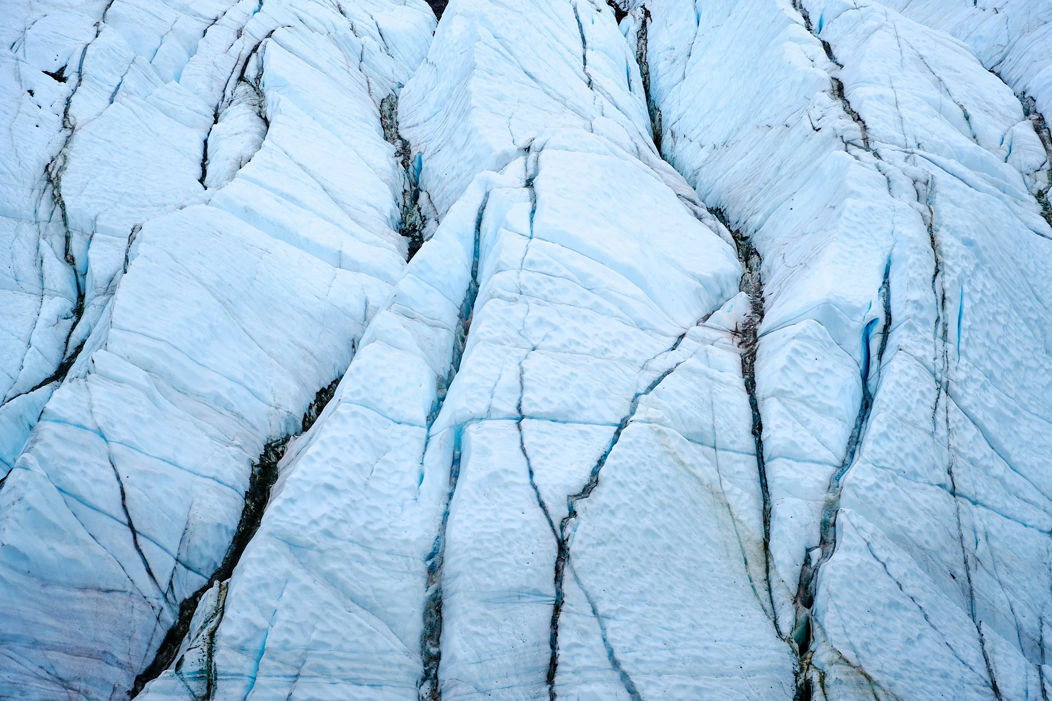 Close-up of a glacier showing deep crevasses and textured ice surface.