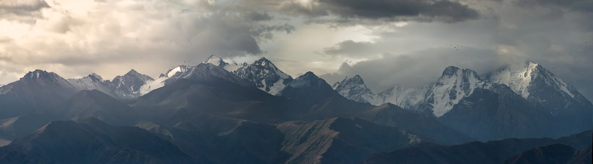 A panoramic view of snow-capped mountains under a cloudy sky.