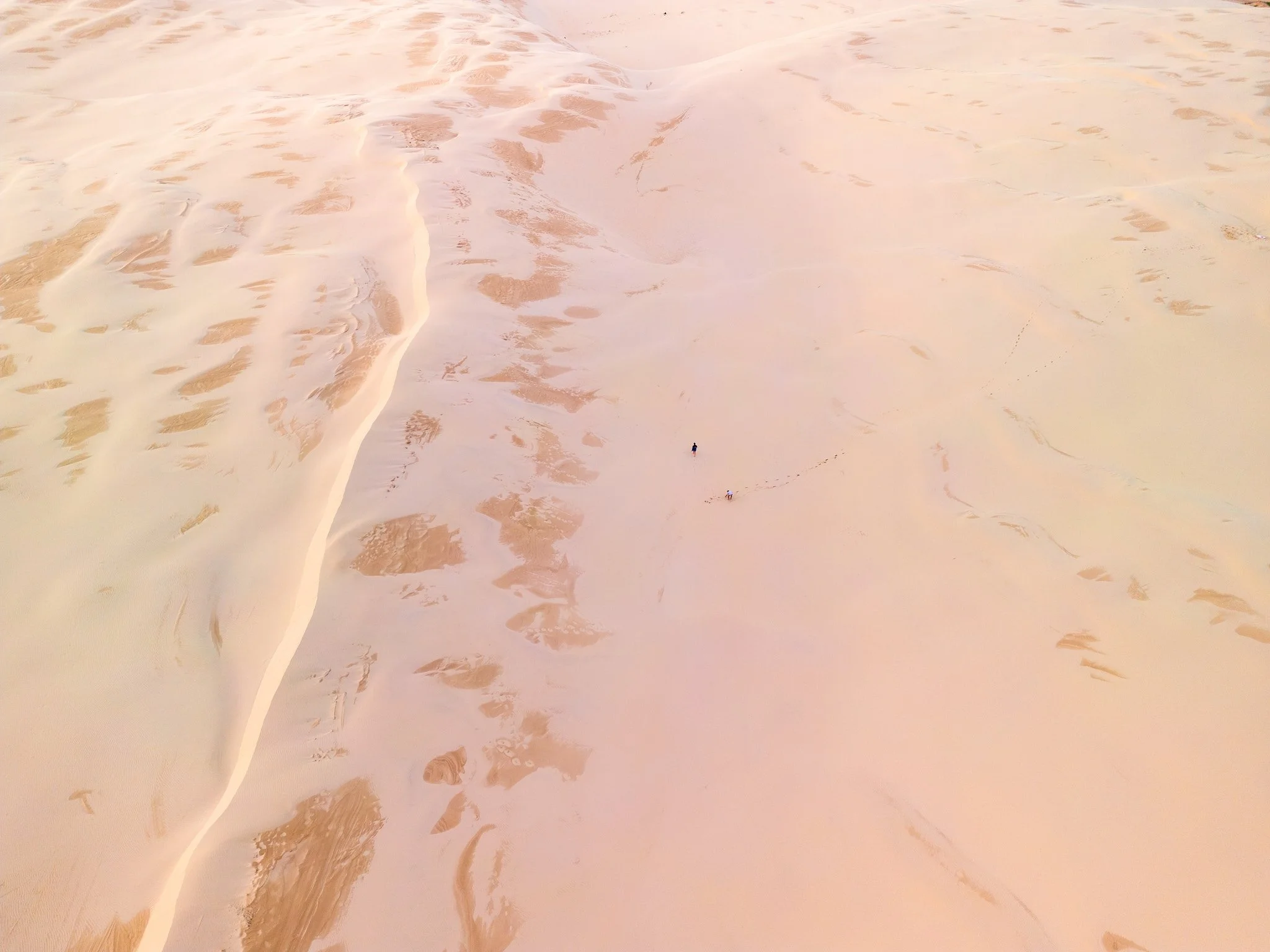 Aerial view of a desert with sand dunes and two small people walking across the sandy terrain. Port Stephens Australia