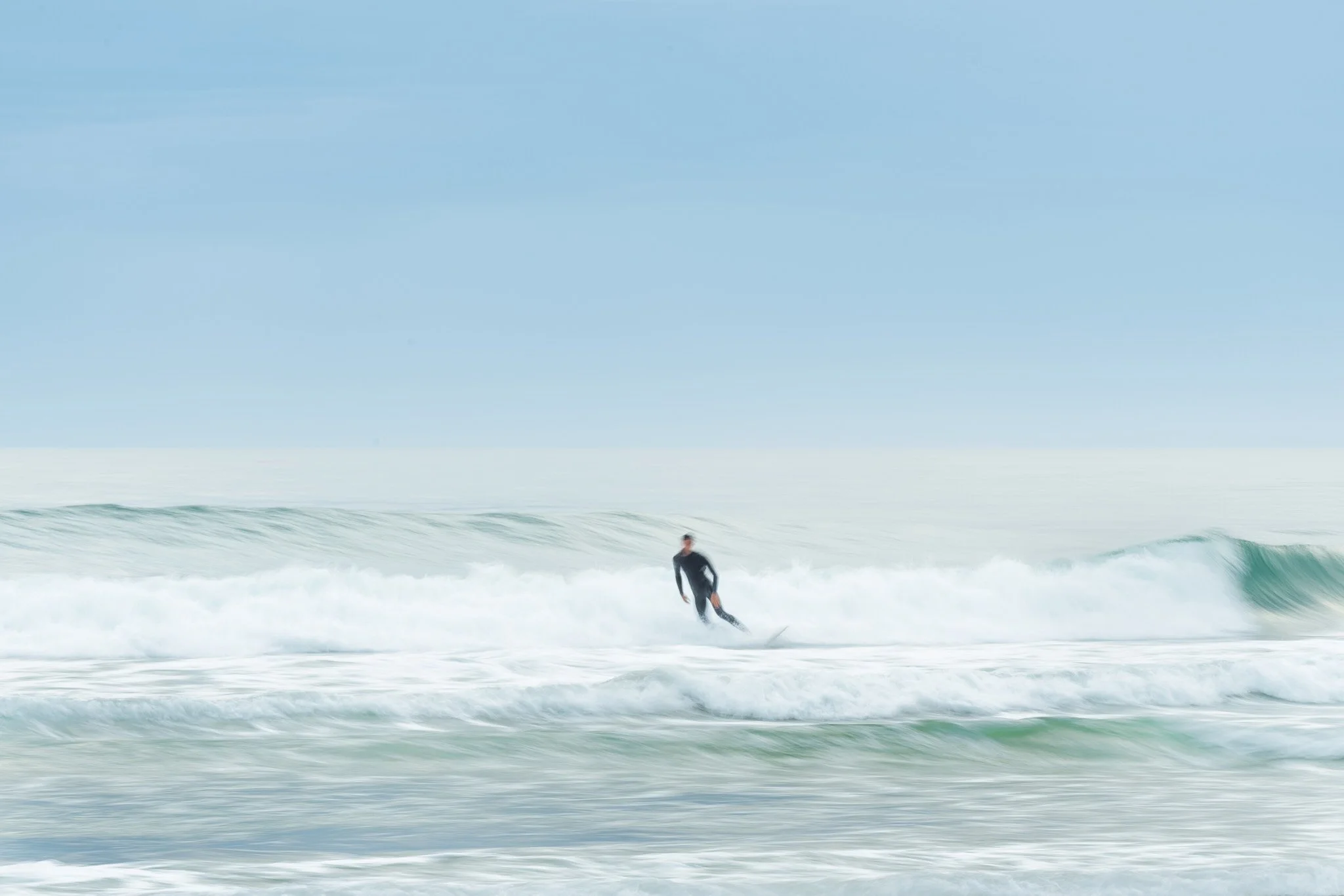 A person in a wetsuit surfing on a wave in the ocean under a blue sky.
