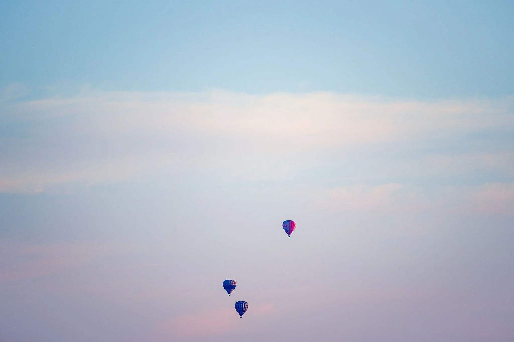 Three hot air balloons floating in the sky during sunset or early evening.