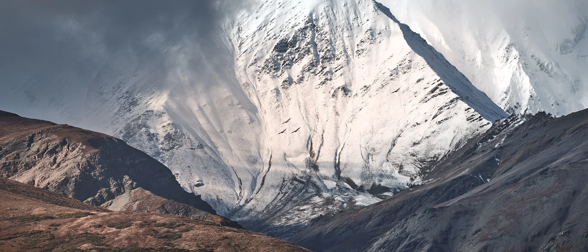 Snow-covered mountain with glaciers and rocky slopes in the foreground.