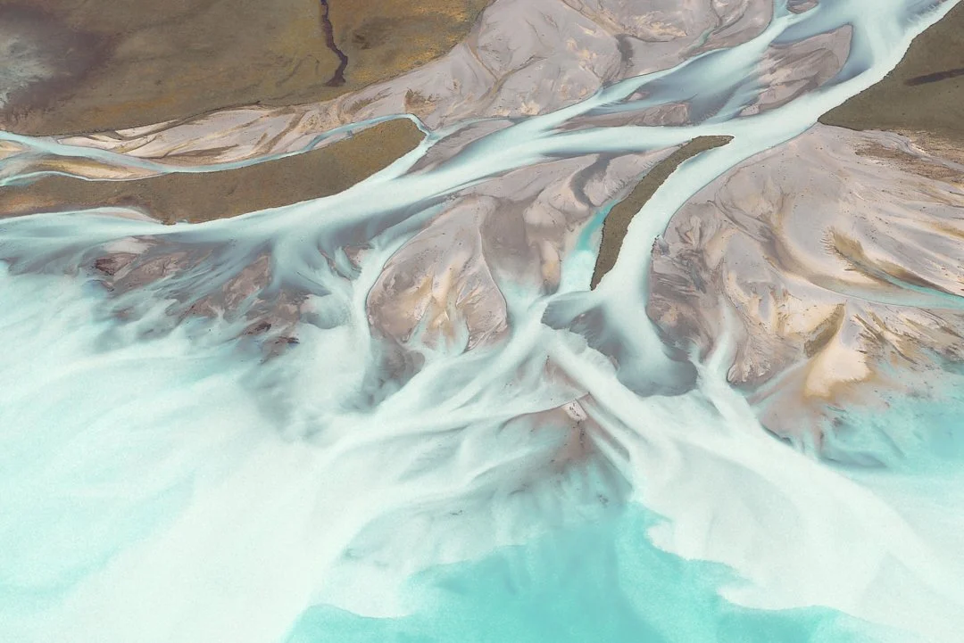 Aerial view of a river with multiple channels flowing through a rugged, mountainous landscape with patches of green and brown terrain.