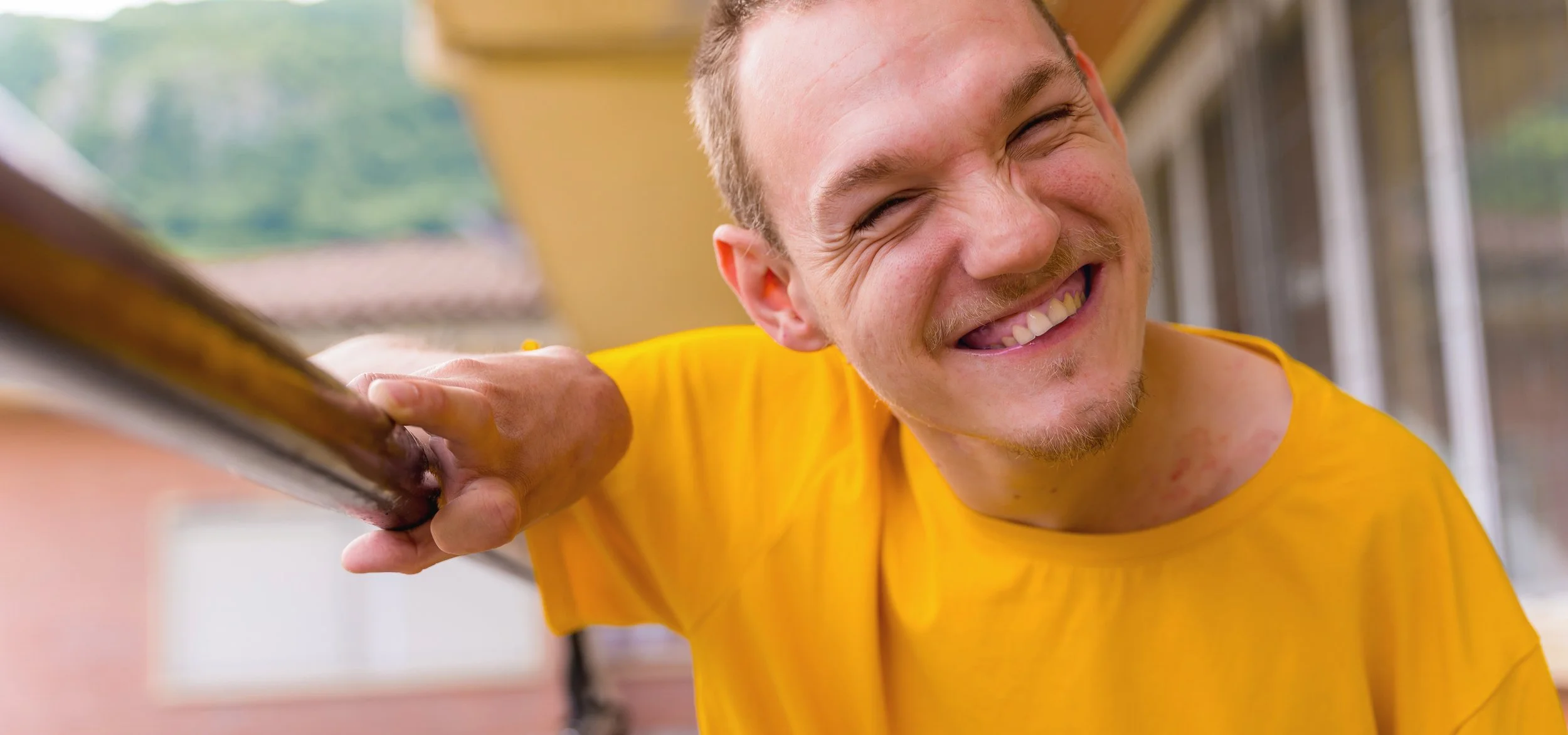 Smiling young man in a yellow shirt holding a support bar outdoors, symbolising independence, empowerment and disability support services through Nursing Group in NSW.