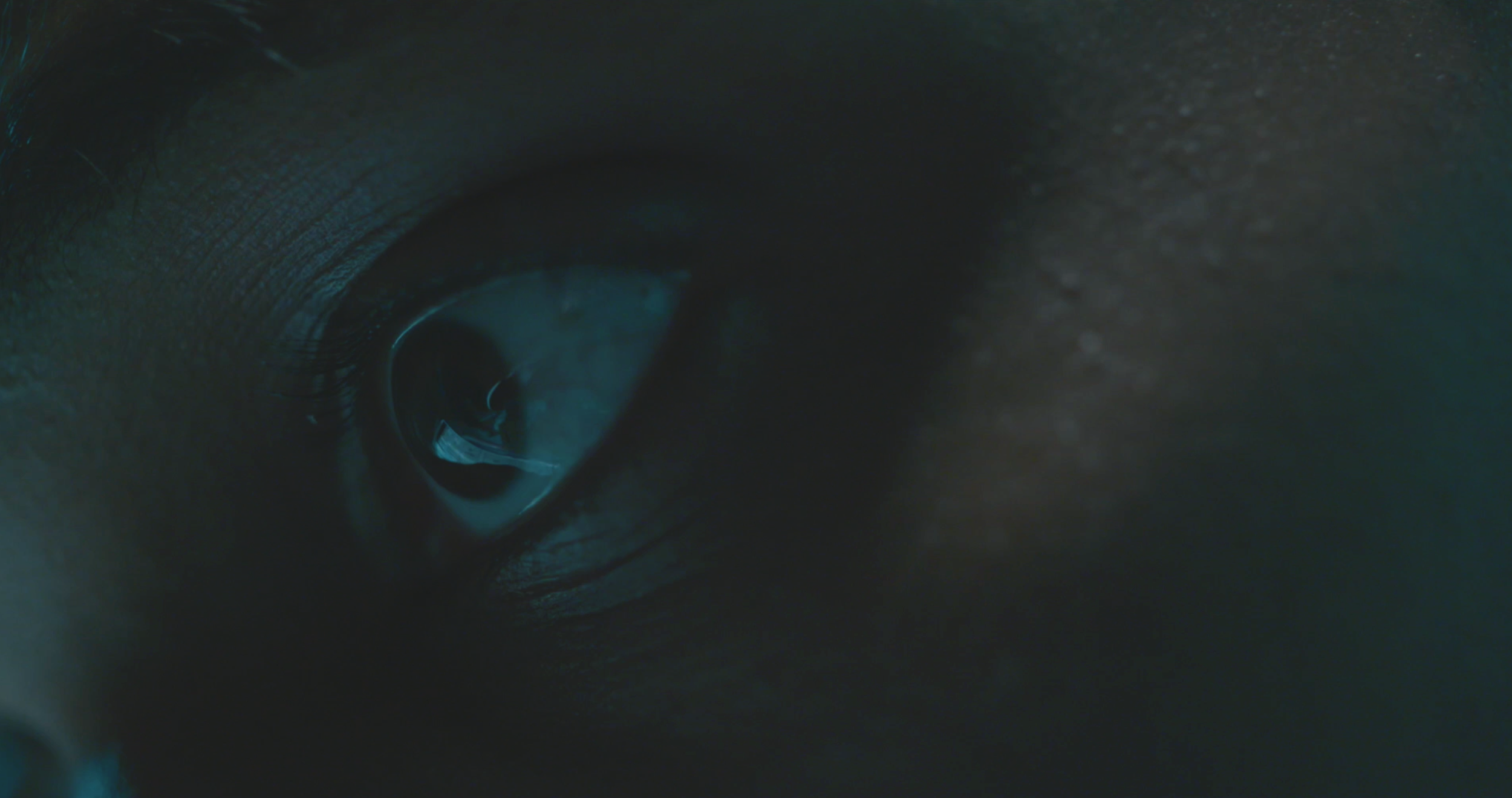 Close-up of a human eye with a reflection of a computer screen in the iris, showing a dark and moody atmosphere.