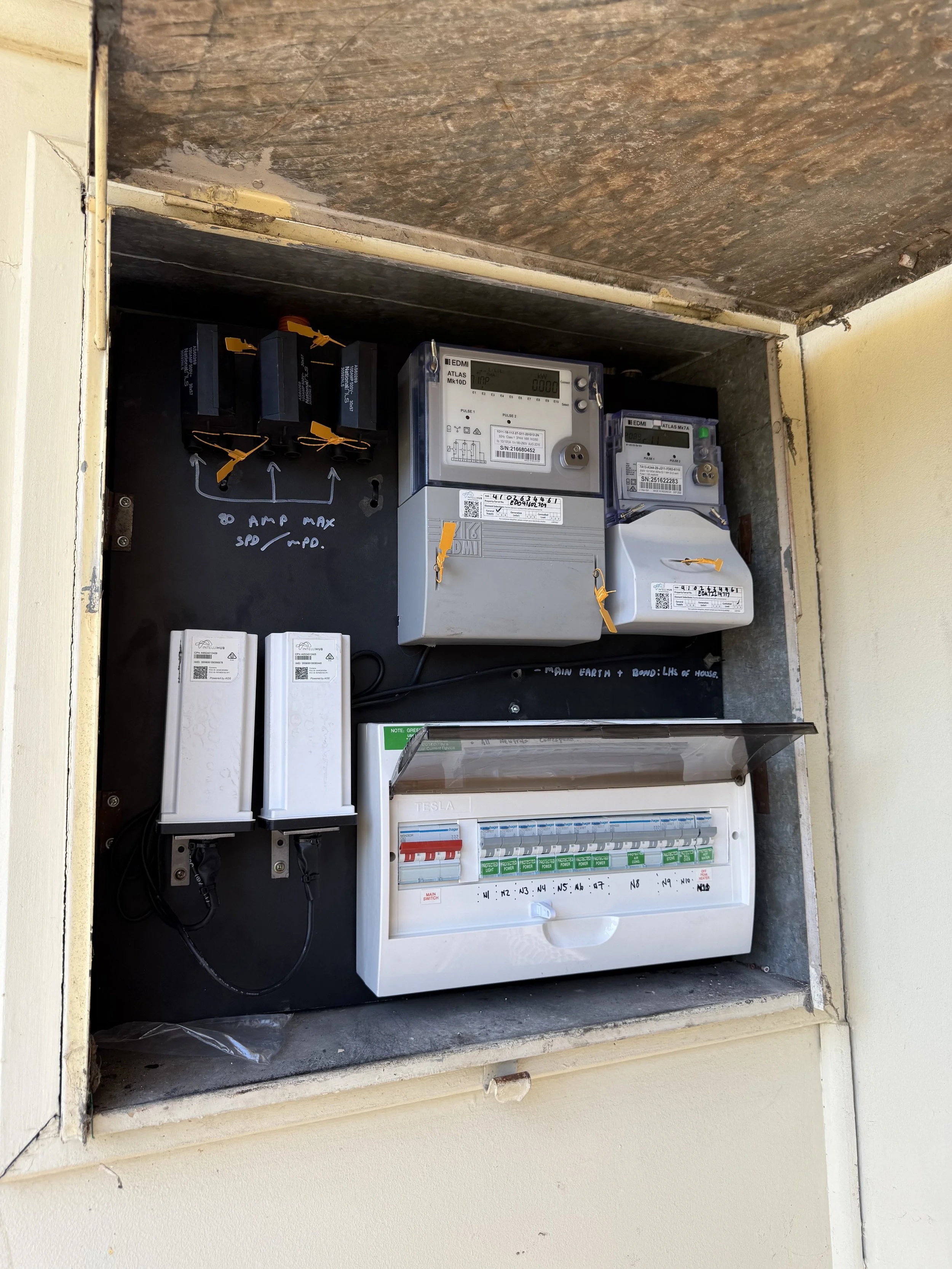 An electrical circuit breaker box mounted on a black surface with a transparent cover and multiple switches and labels inside.