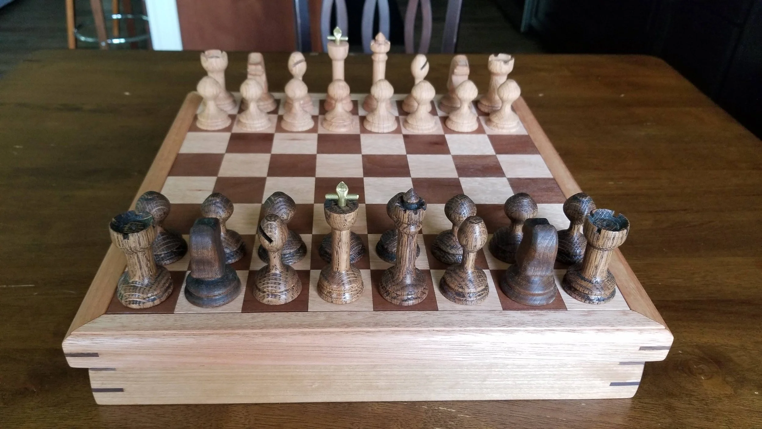 Wooden chessboard with chess pieces set up for starting a game, on a wooden table.